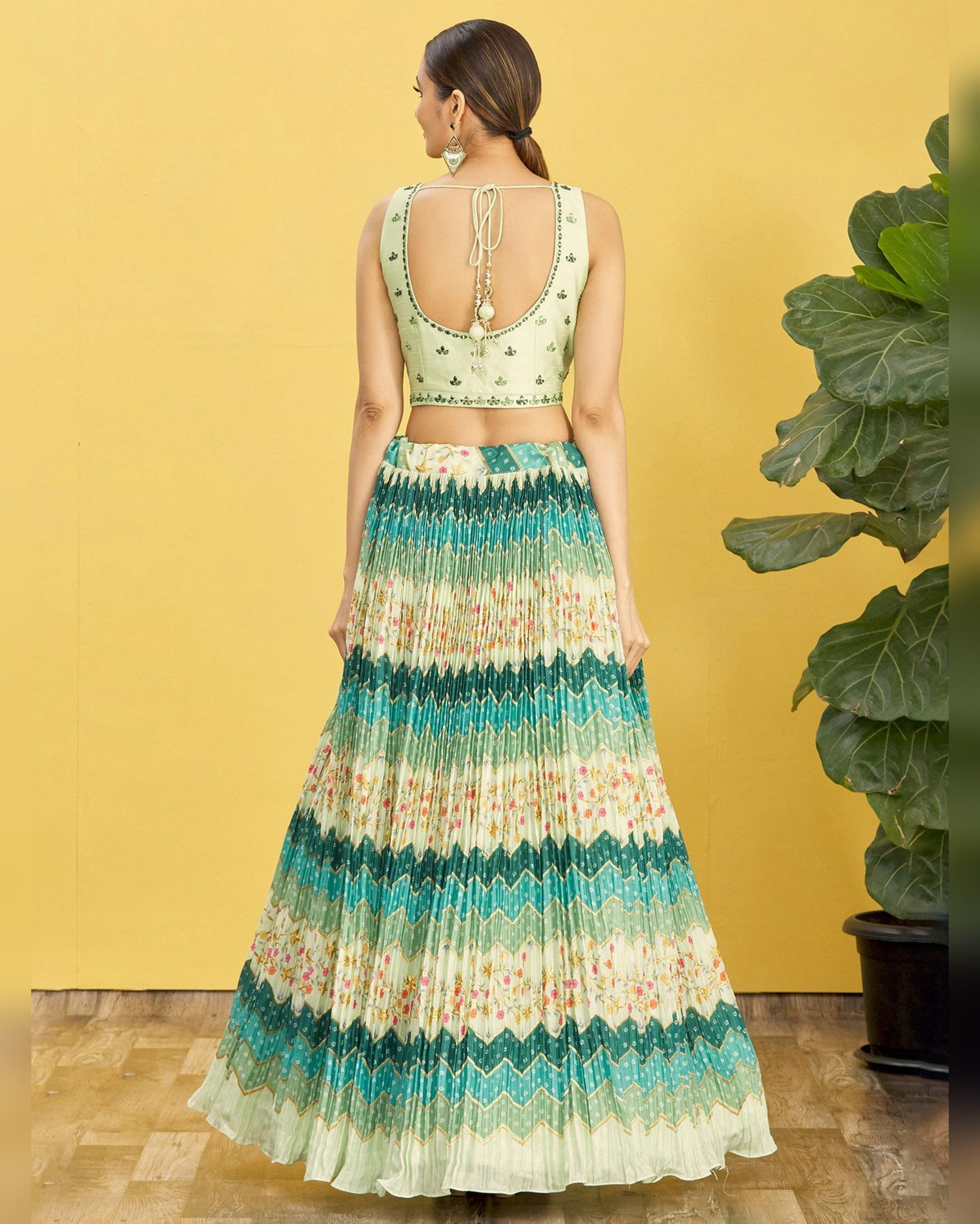 Woman wearing a green and white patterned outfit against a yellow wall.