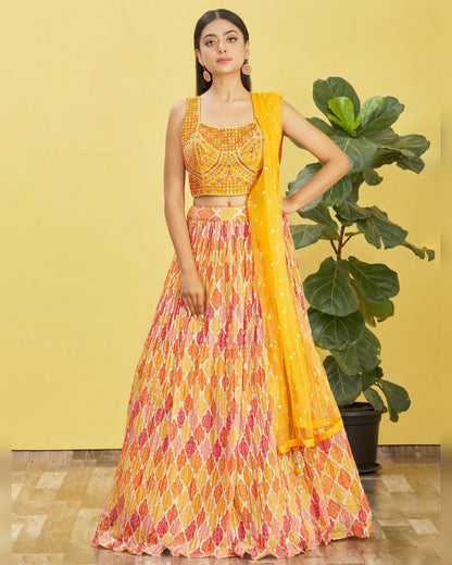 Woman wearing a colorful traditional outfit with a yellow dupatta against a yellow wall.
