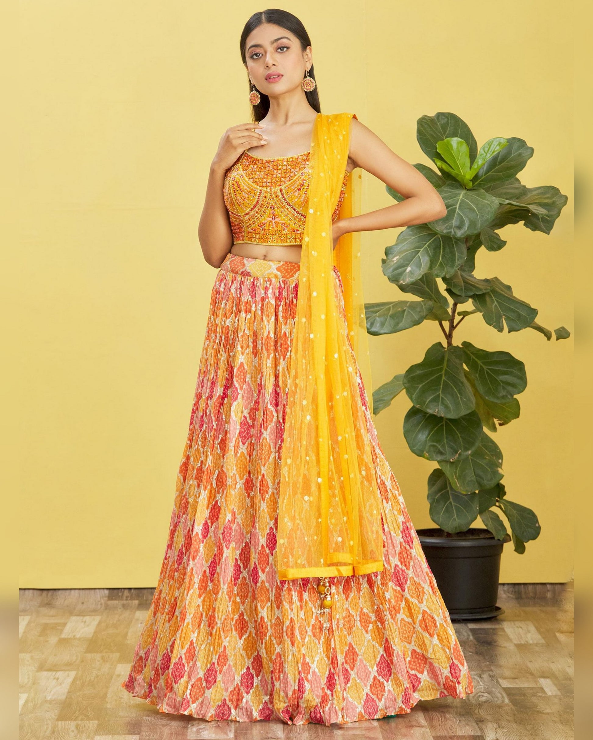 Woman in a yellow and patterned outfit standing against a yellow wall with a plant.