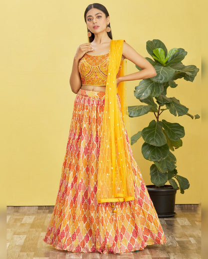 Woman in a yellow and patterned outfit standing against a yellow wall with a plant.