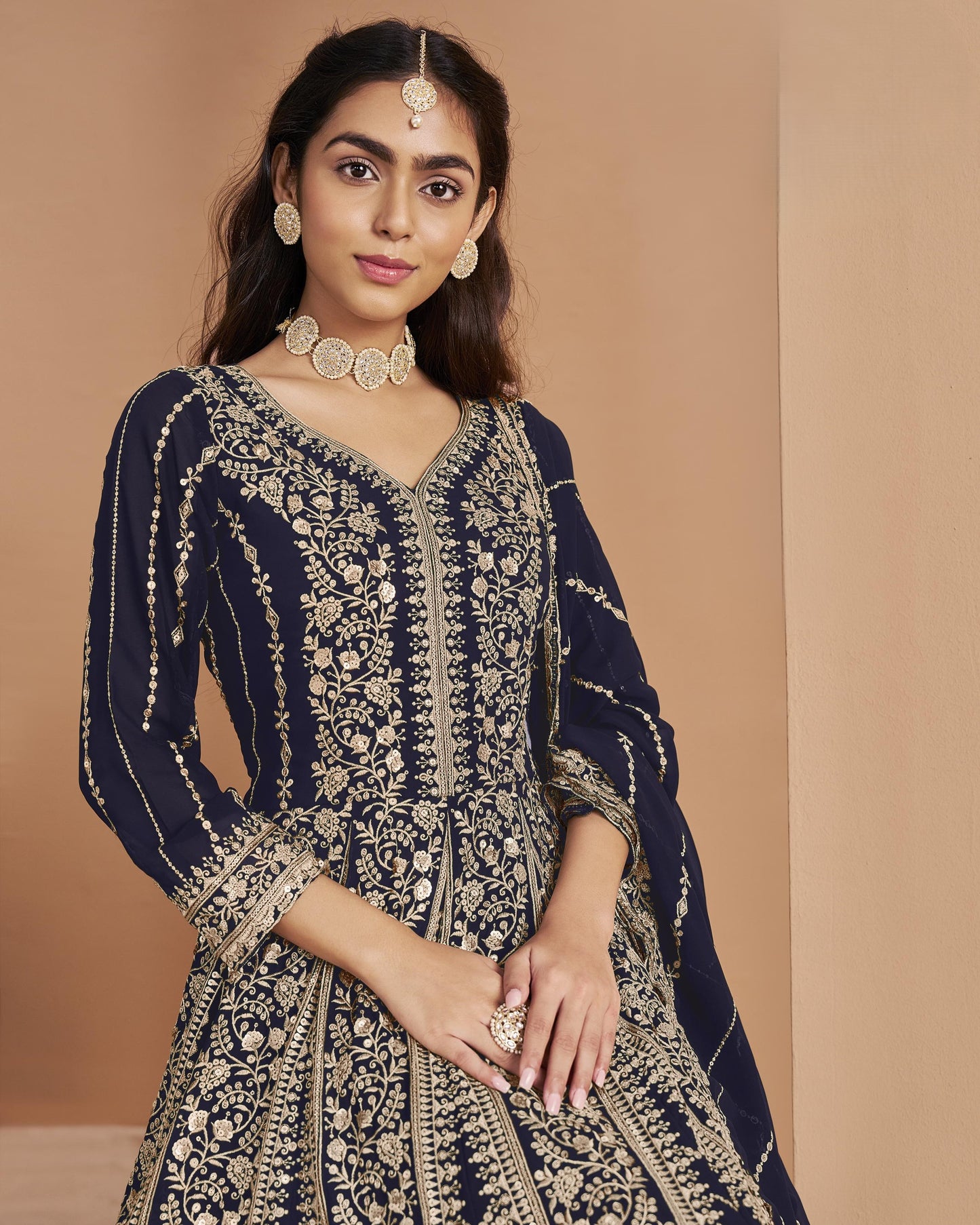 Woman wearing a navy blue and gold embroidered traditional outfit against a beige background