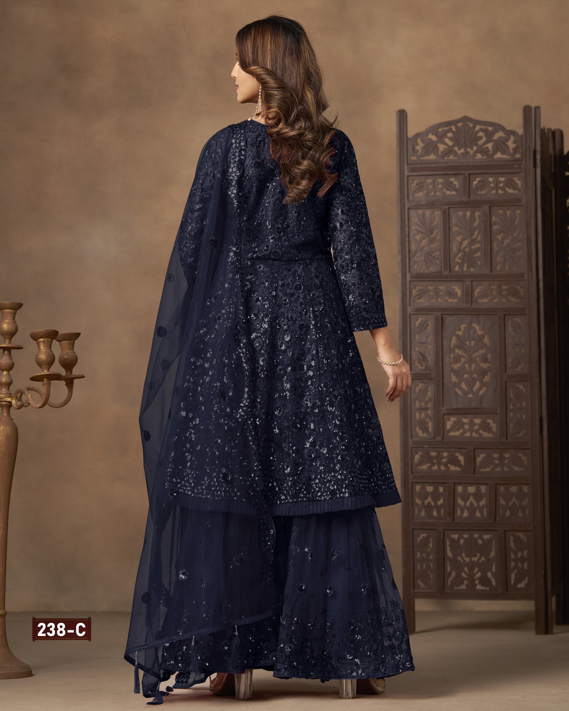 Woman wearing a dark blue embroidered traditional outfit in a decorated room.