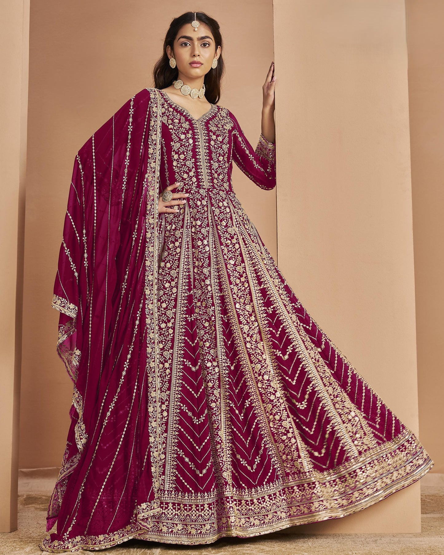 Woman wearing a maroon embroidered traditional outfit with a beige background