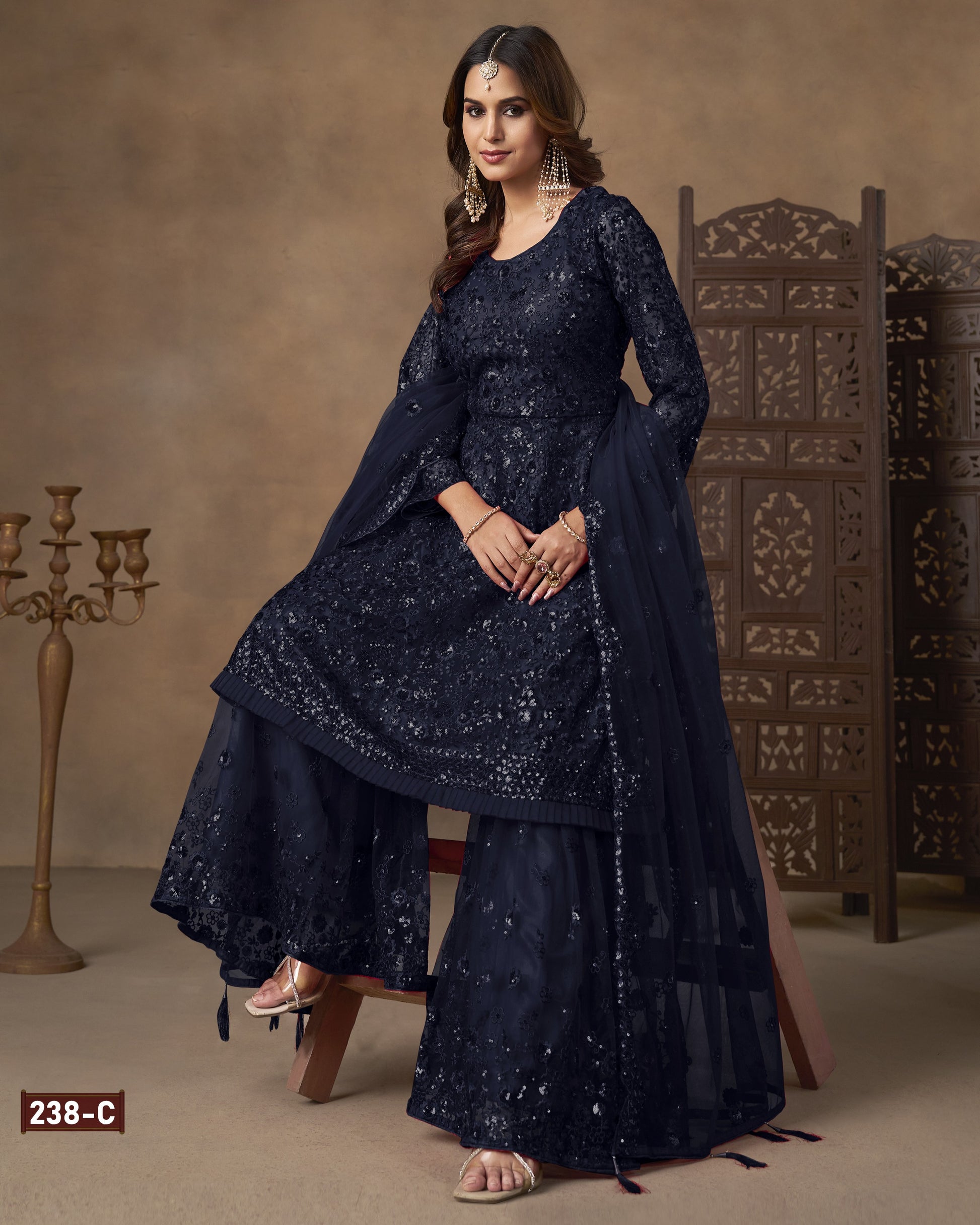 Woman wearing a dark blue embroidered traditional outfit with a brown background