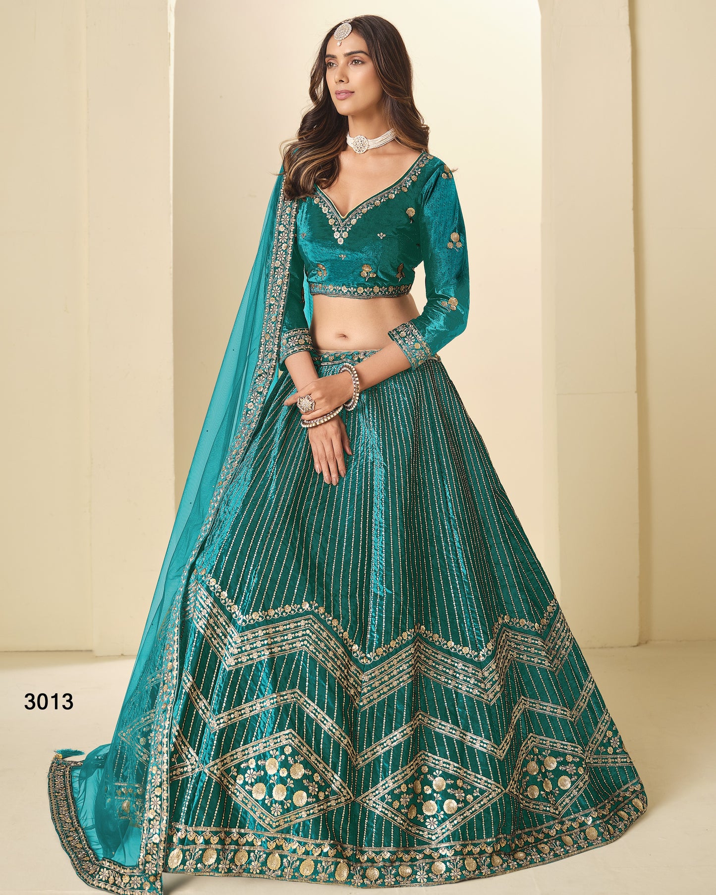 Woman wearing a teal embroidered lehenga with a matching dupatta against a beige background