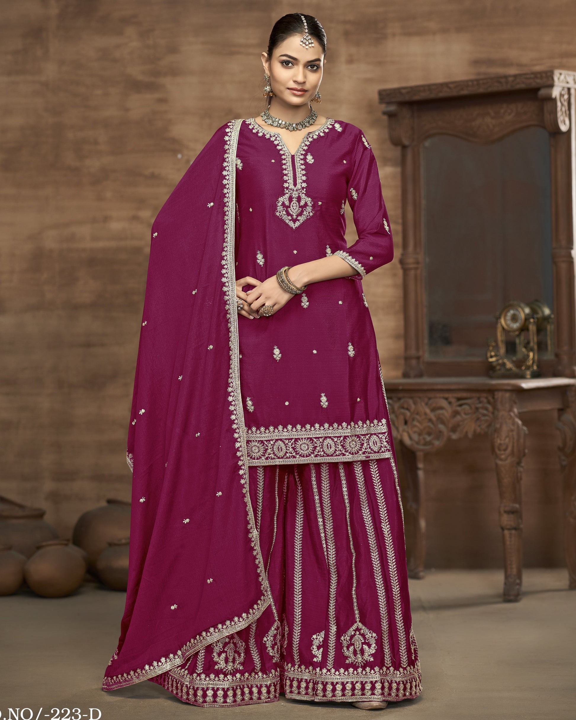Woman wearing a traditional pink outfit with intricate white embroidery in a warm-toned room.