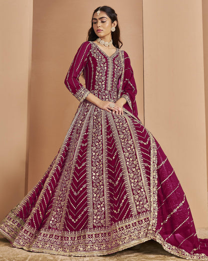 Woman wearing a maroon and gold embroidered traditional outfit against a beige background