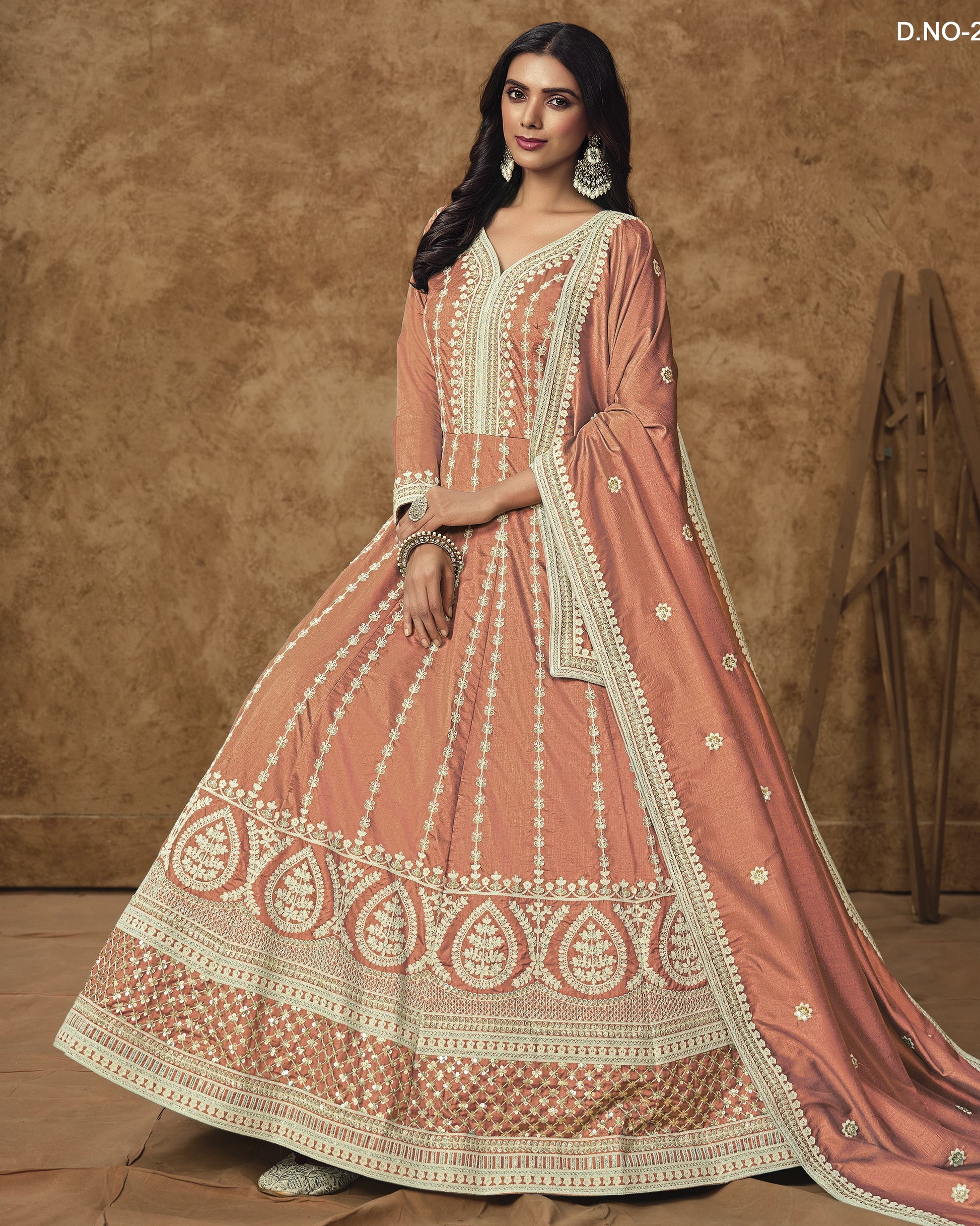 Woman wearing a traditional pink and gold embroidered outfit against a brown background