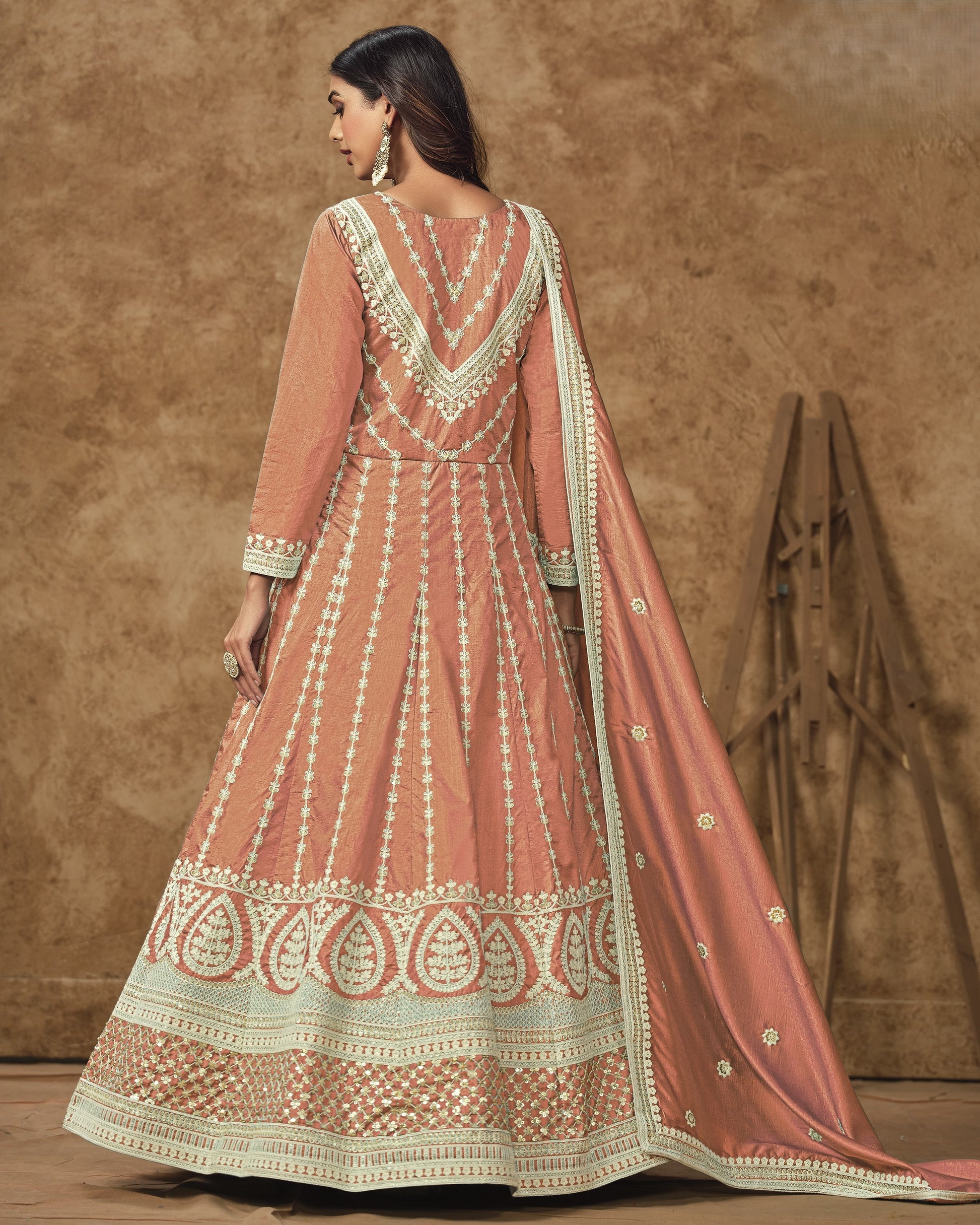 Woman wearing a traditional pink and white embroidered outfit against a brown background