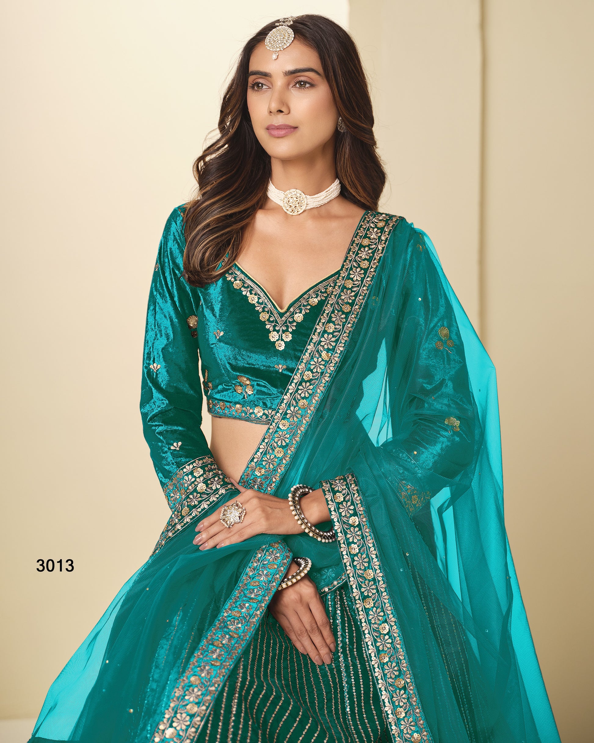 Woman wearing a teal traditional outfit with intricate designs on a beige background
