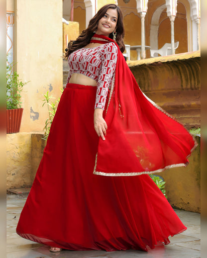 Woman wearing a red and white traditional outfit with a flowing red dupatta in an outdoor setting.