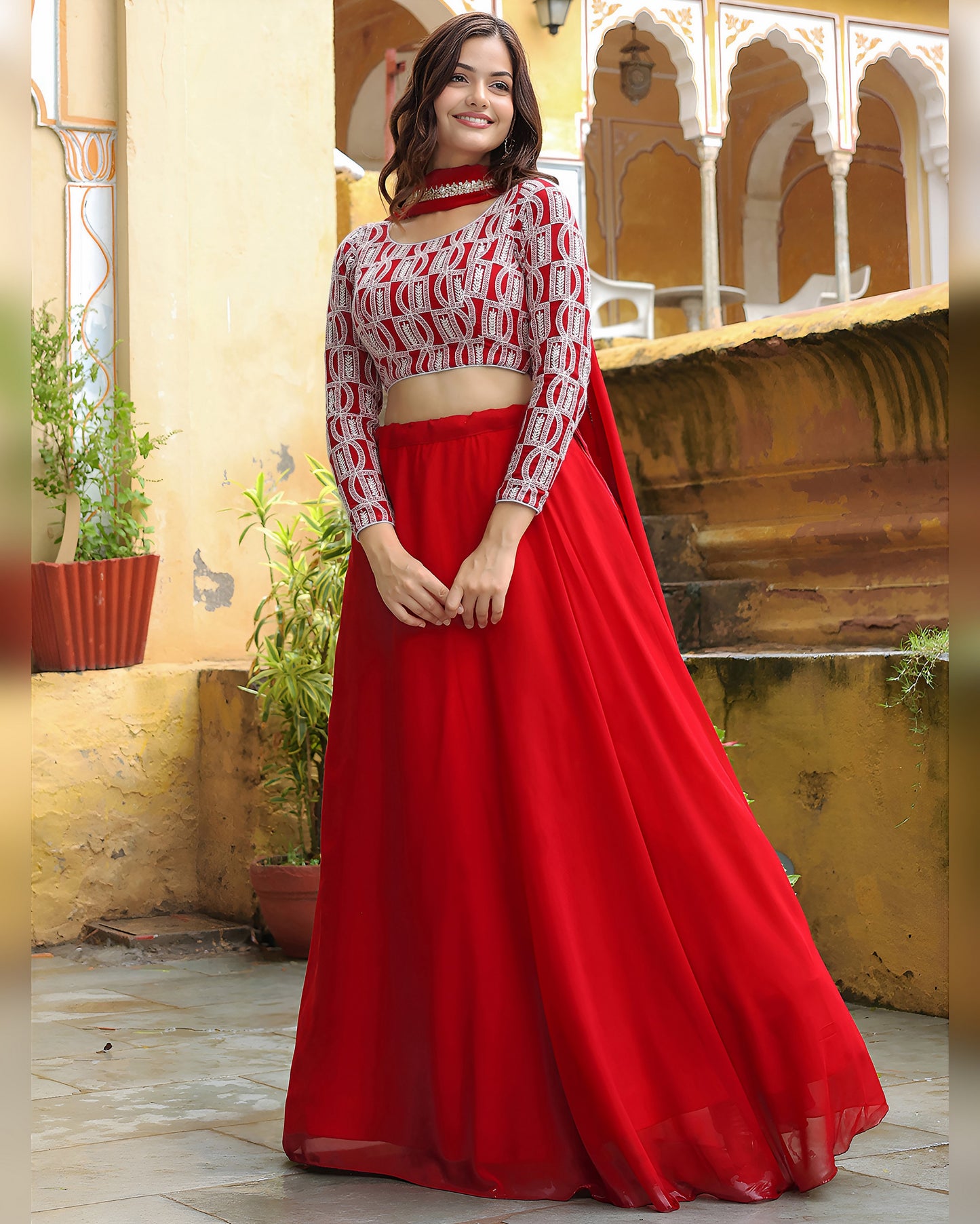 Woman wearing a red and white traditional outfit in an outdoor setting with architectural elements.