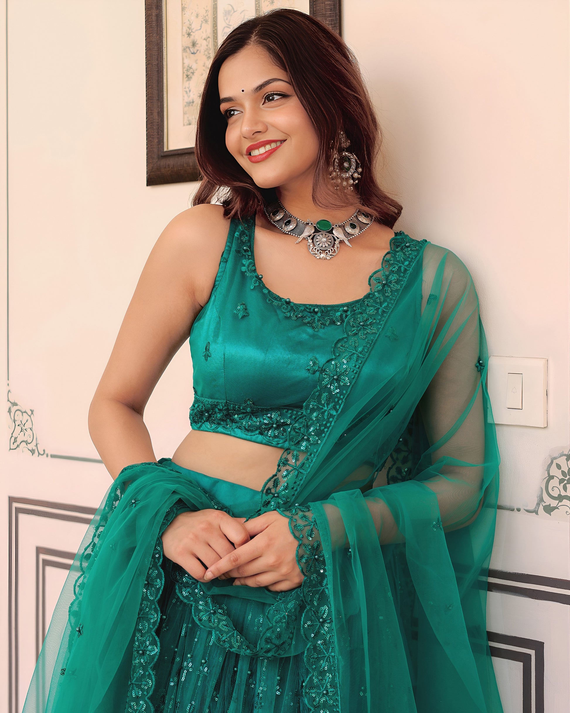 Woman wearing a green traditional outfit with jewelry indoors.