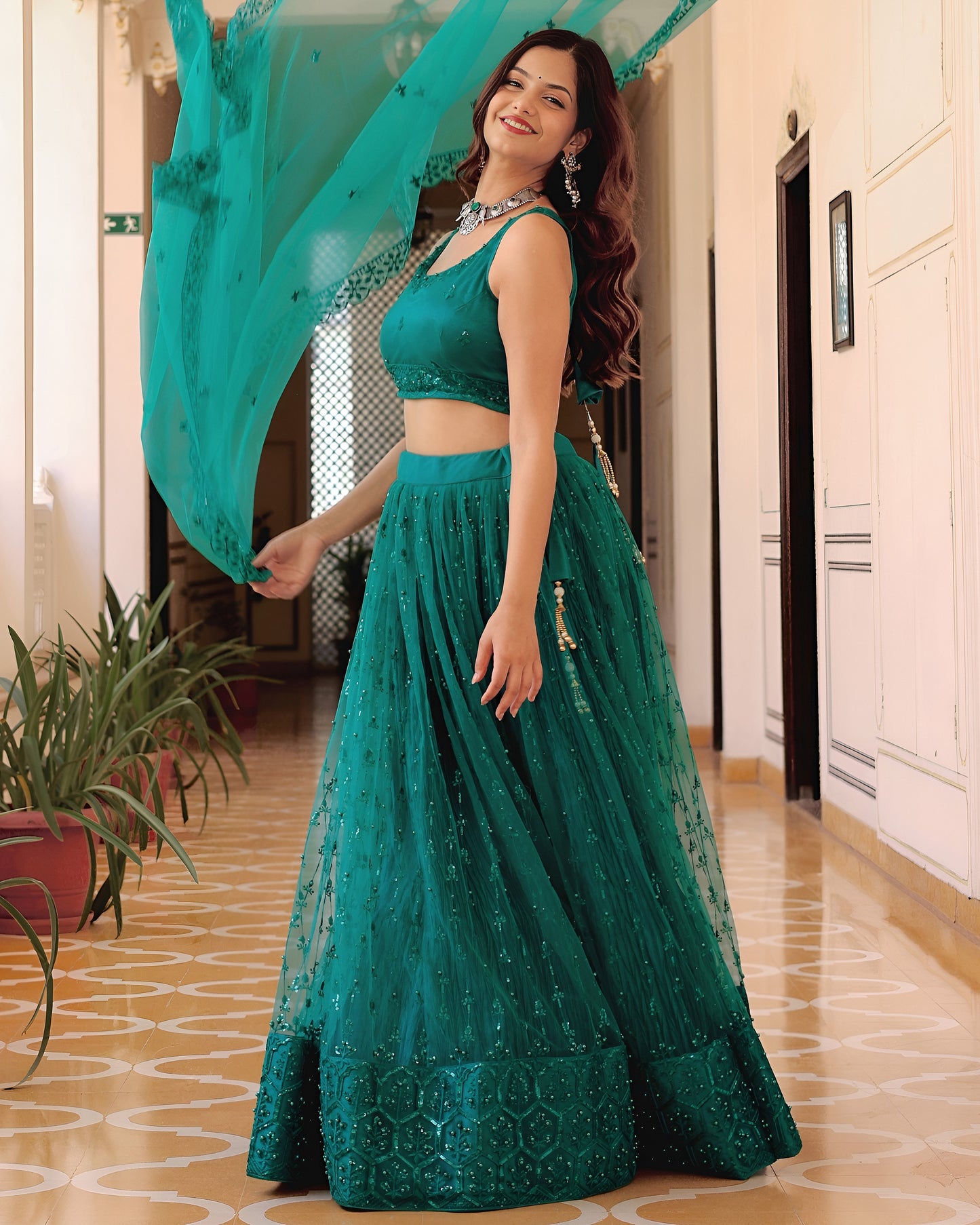 Woman in a teal traditional outfit with a flowing dupatta in an indoor setting.