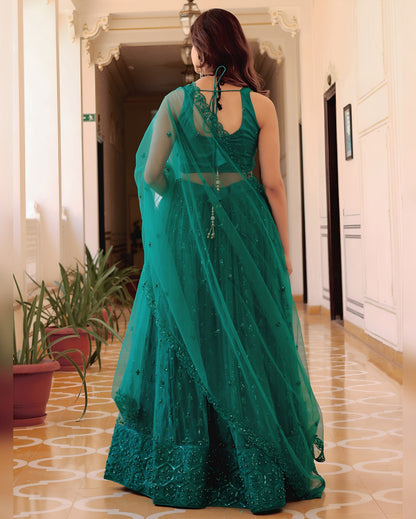 Woman in a teal saree standing in a hallway with plants and a door in the background.