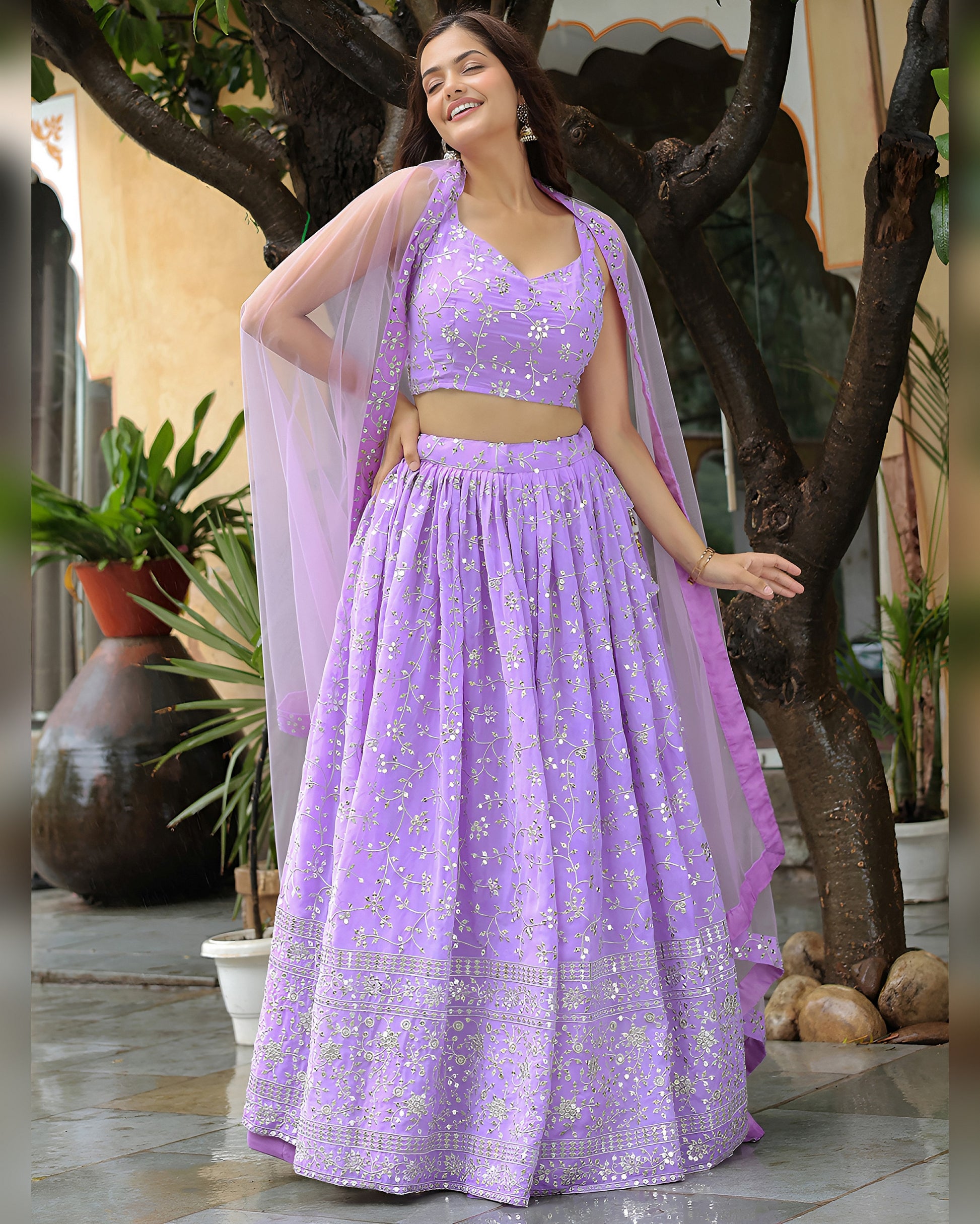 Woman in a purple traditional outfit standing outdoors with plants in the background