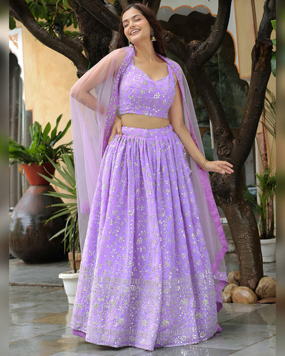 Woman in a purple traditional outfit standing outdoors with plants in the background