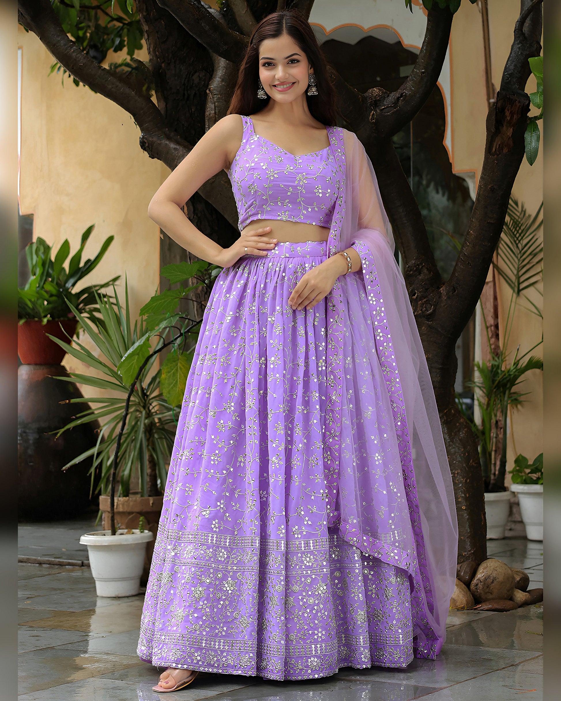 Woman in a purple traditional outfit standing outdoors with plants in the background