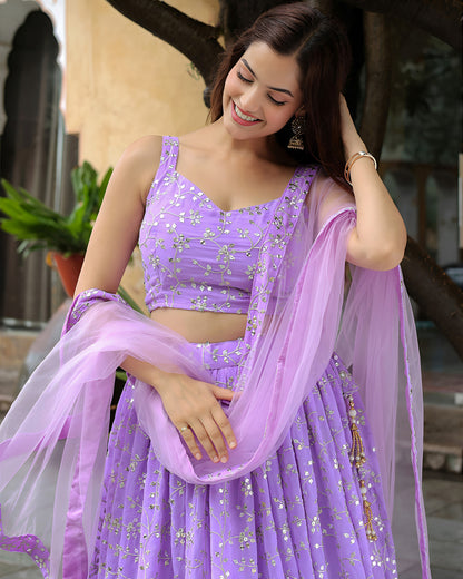 Woman in a purple traditional outfit with a matching dupatta, standing outdoors.