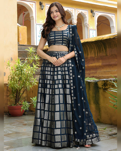 Woman in a traditional outfit with a checkered pattern standing in an outdoor setting.