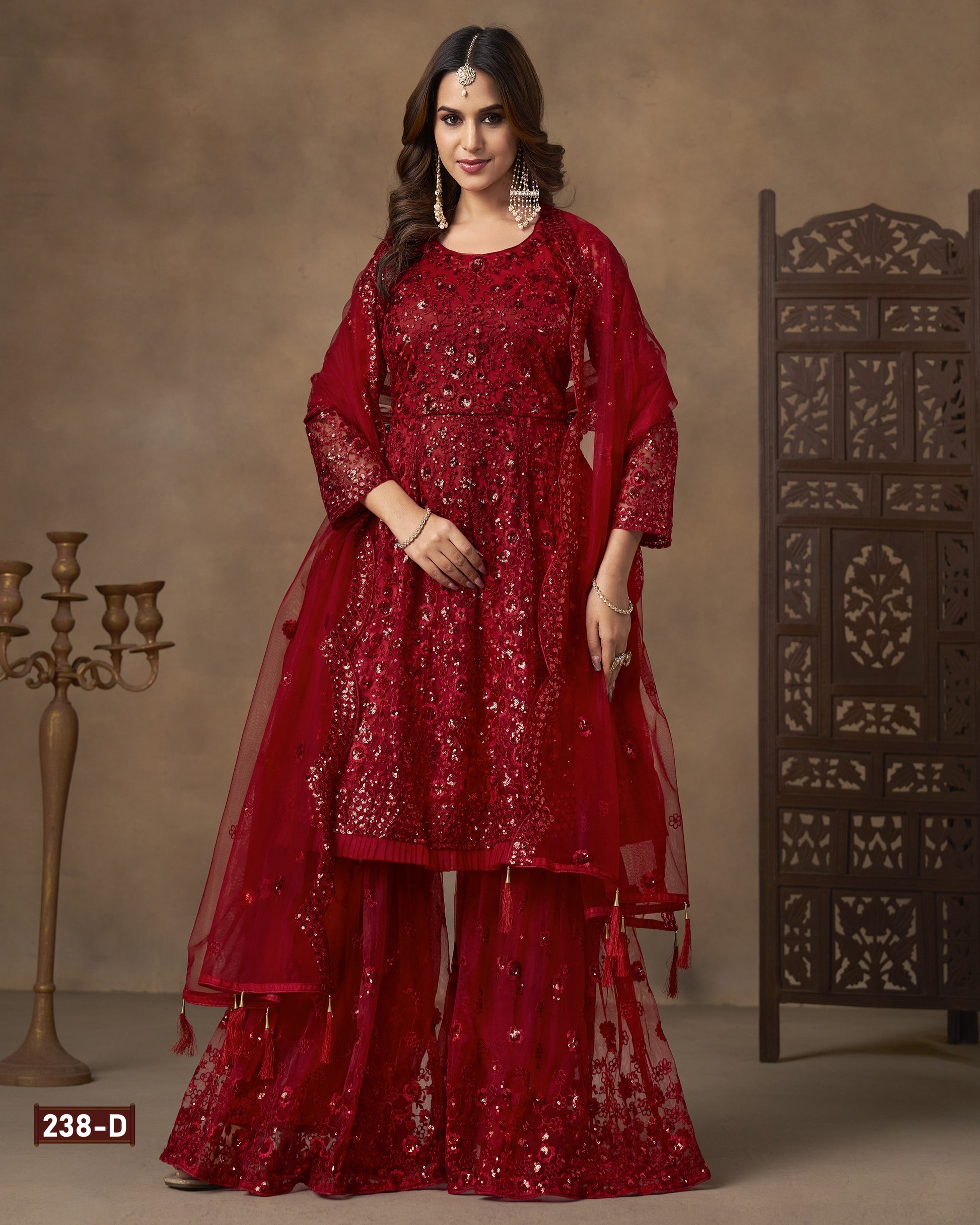 Woman wearing a red traditional outfit with a matching dupatta against a neutral background