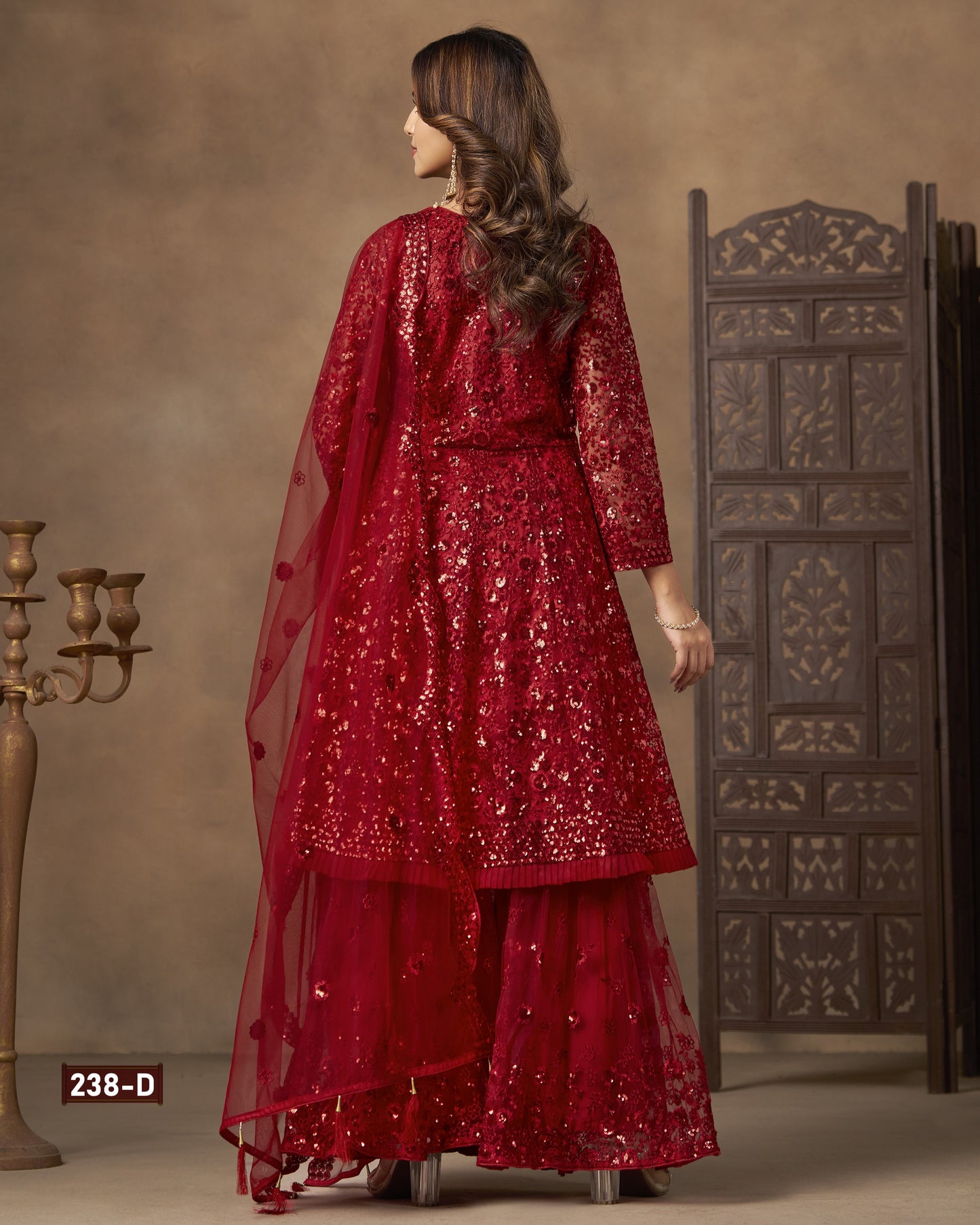 Woman in a red sequined outfit standing against a textured wall with a decorative screen.