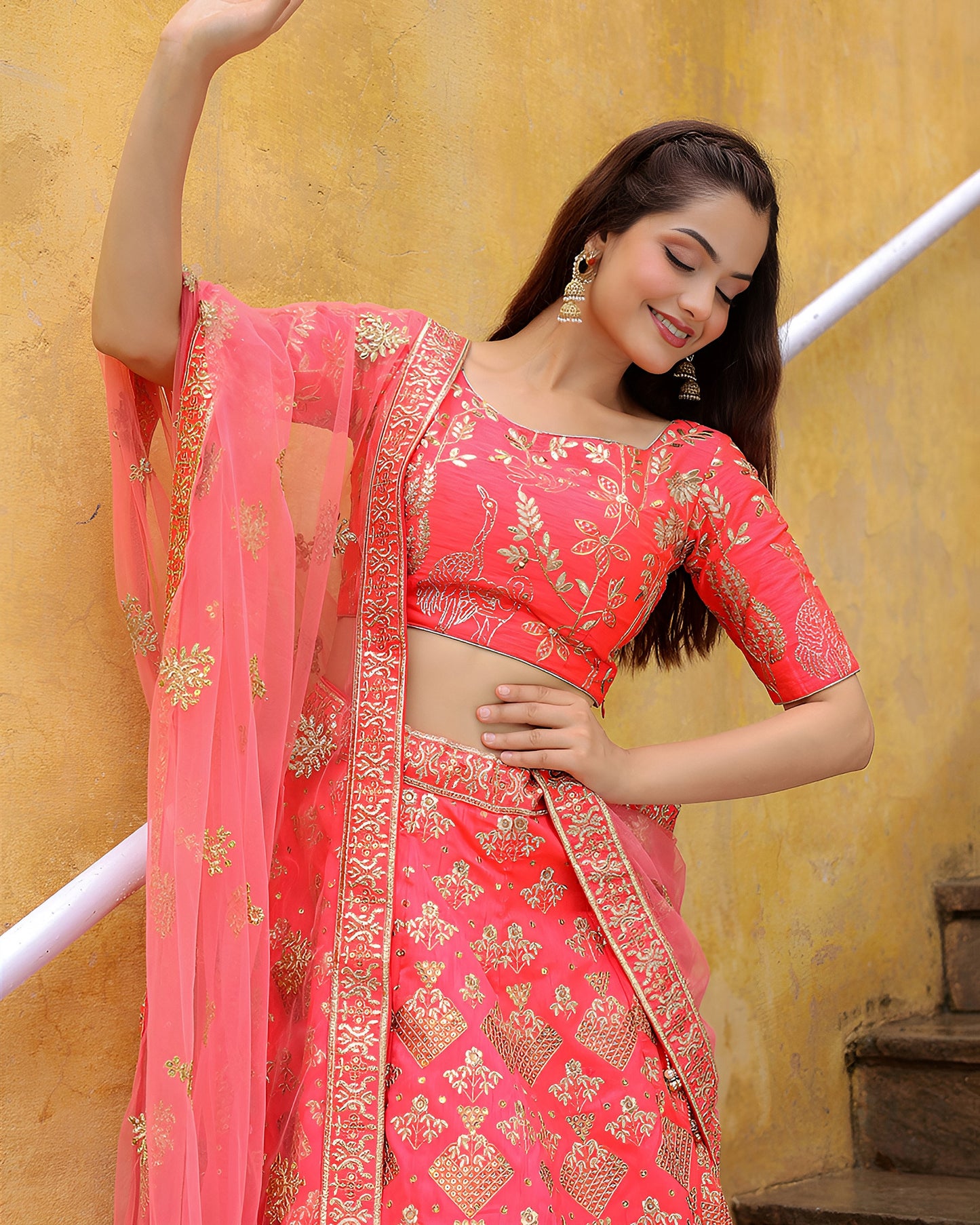 Woman in a pink traditional outfit with gold patterns against a yellow wall.