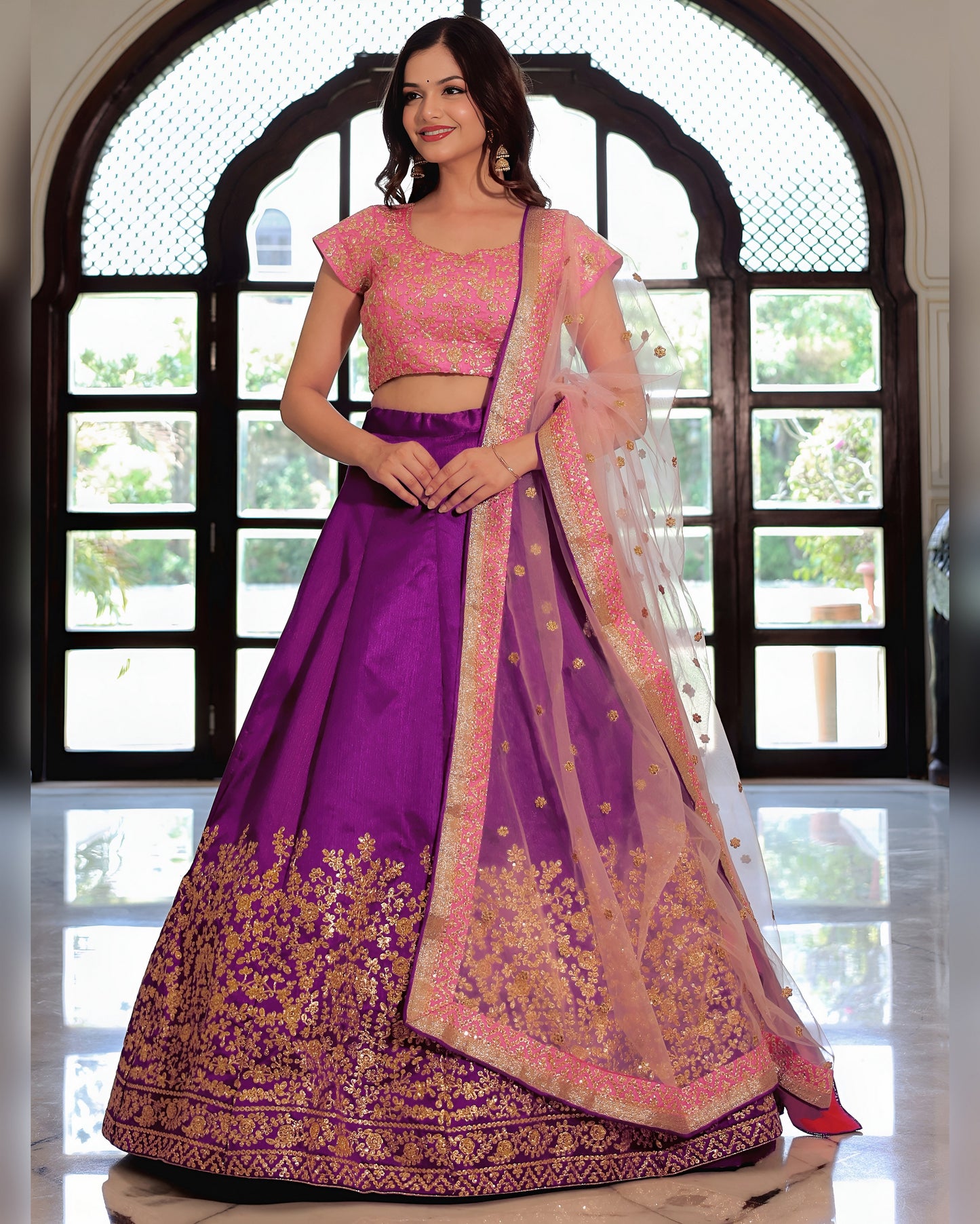 Woman wearing a traditional purple and pink lehenga with a large window in the background
