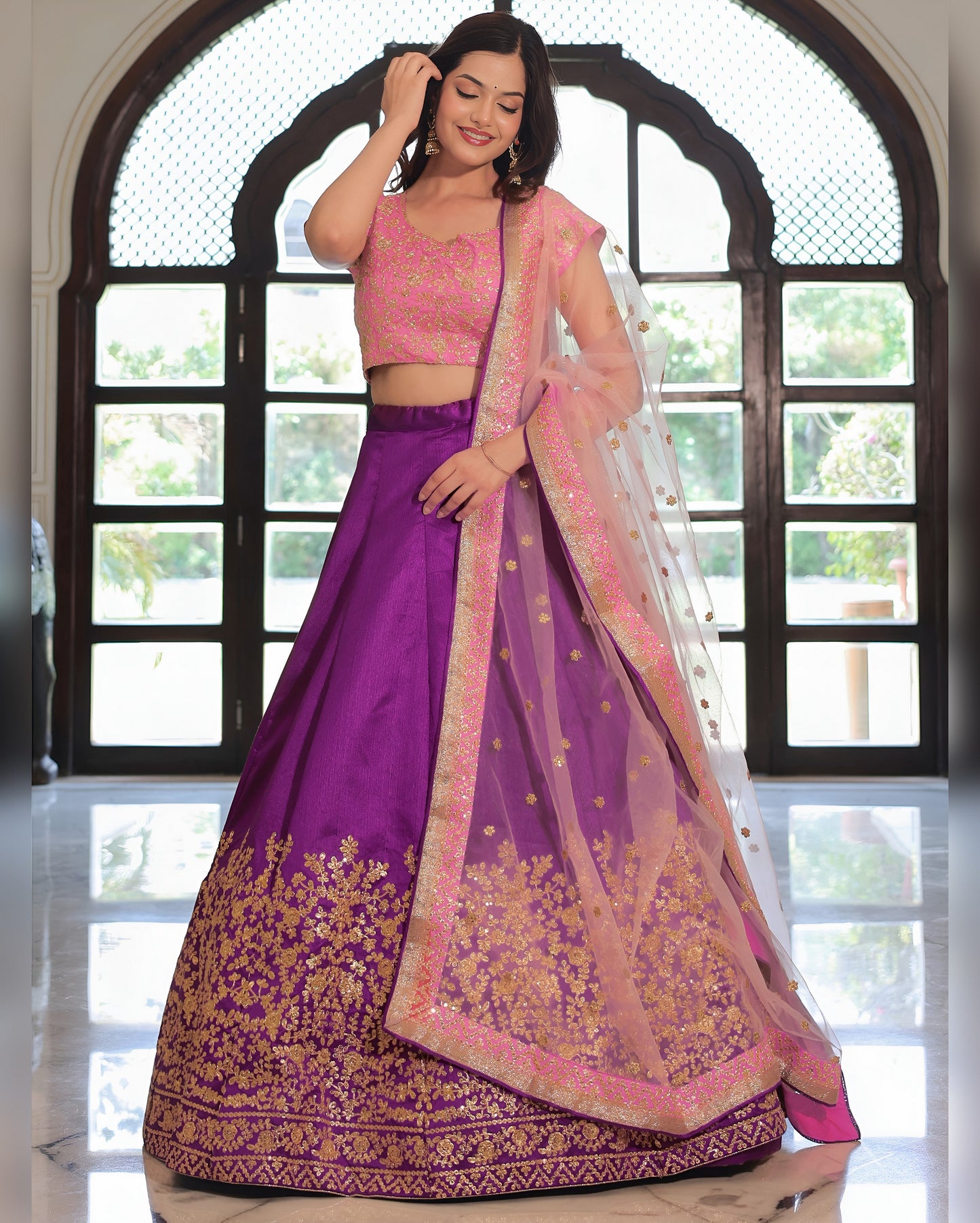 Woman in a purple and pink traditional outfit standing in front of a window.