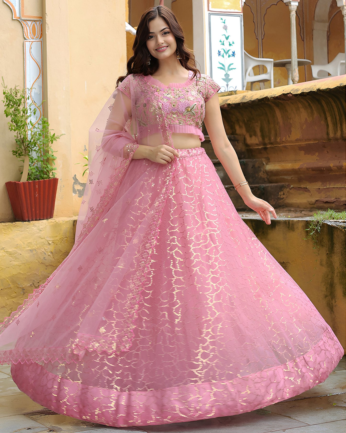 Woman wearing a pink traditional outfit with intricate designs in an outdoor setting.