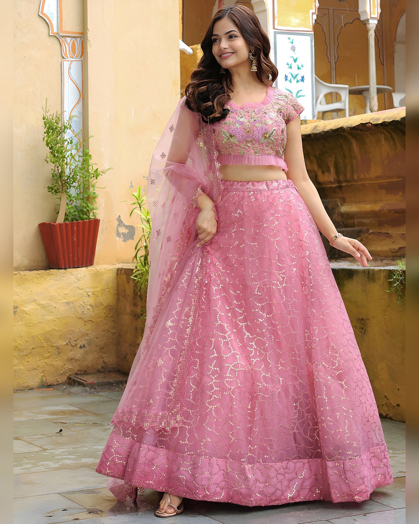 Woman in a pink traditional outfit standing in front of a decorative wall.