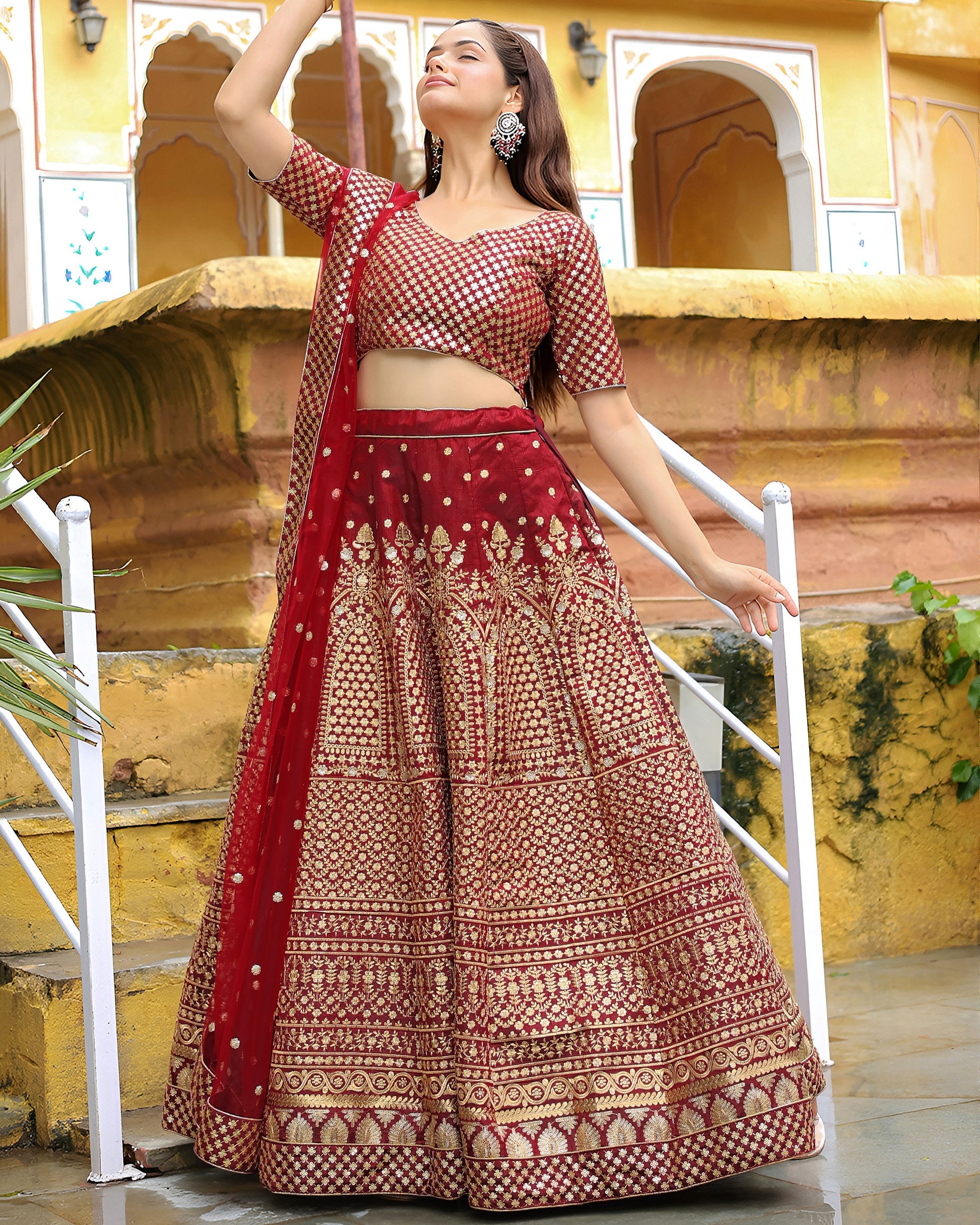 Woman in a red and gold traditional outfit standing in front of a yellow architectural background