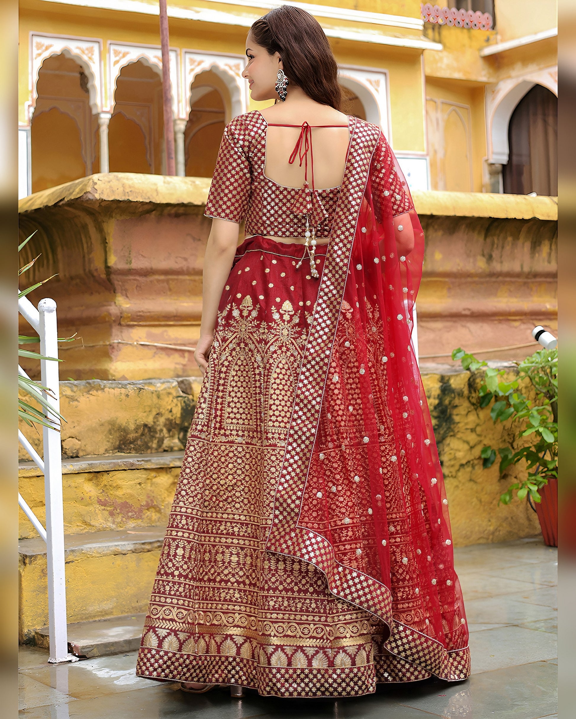 Woman in a red and gold embroidered traditional outfit standing in an ornate indoor setting.