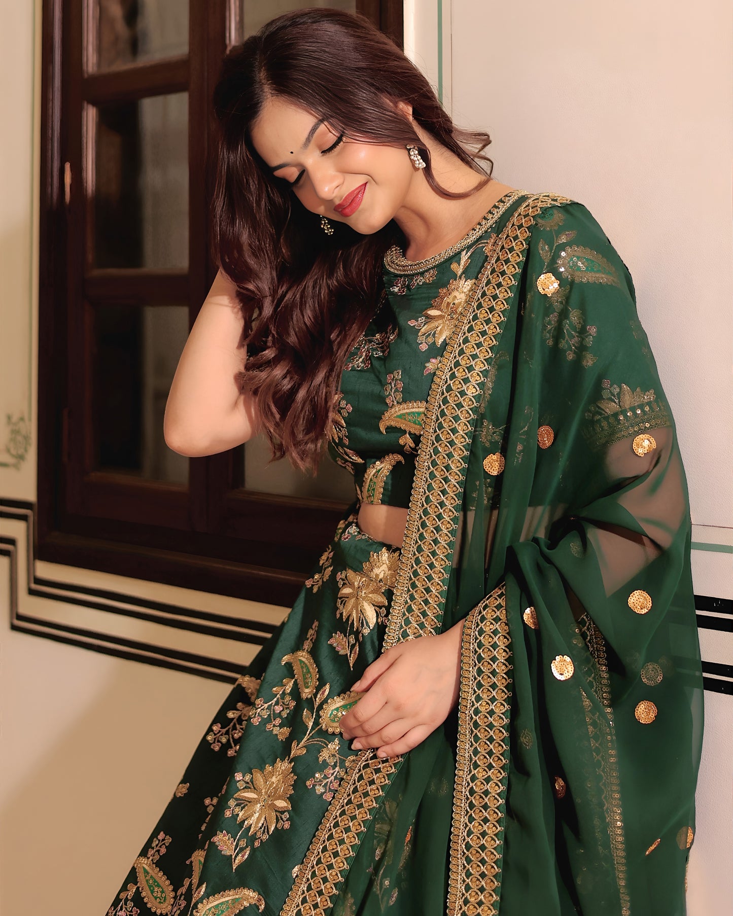 Woman wearing a green embroidered saree with gold details indoors.