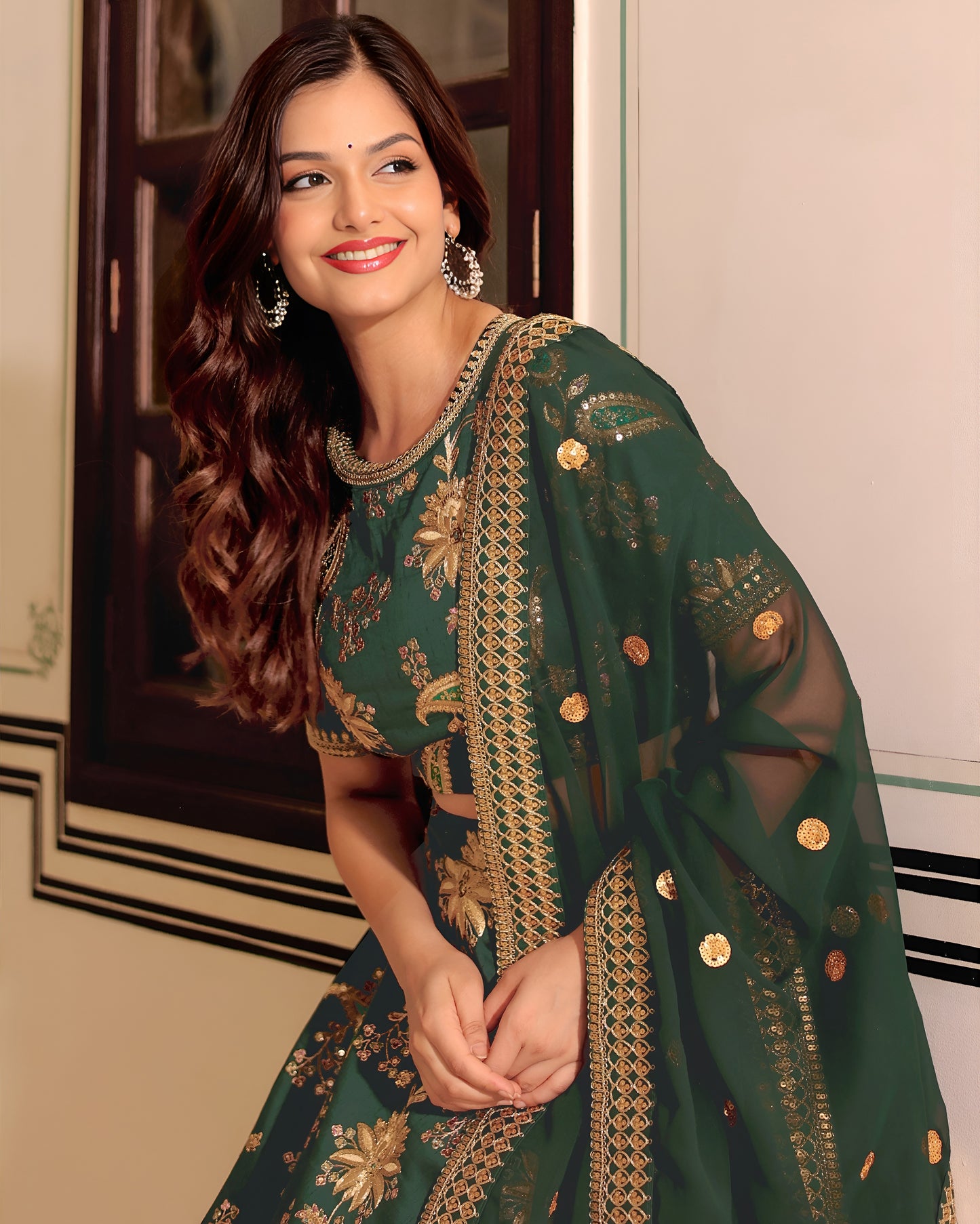 Woman wearing a green traditional outfit with gold embroidery indoors.