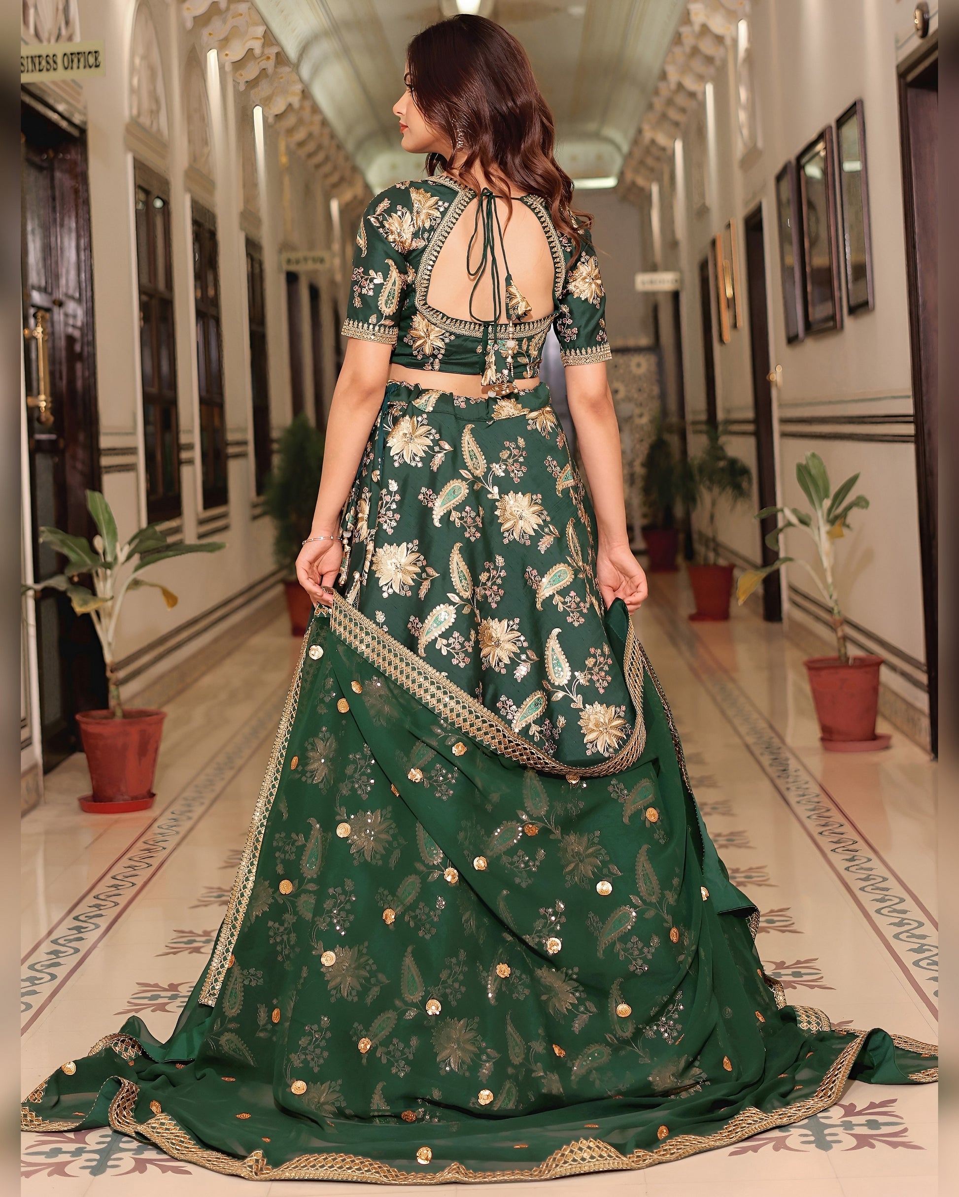 Woman in a green floral traditional outfit walking down a hallway.