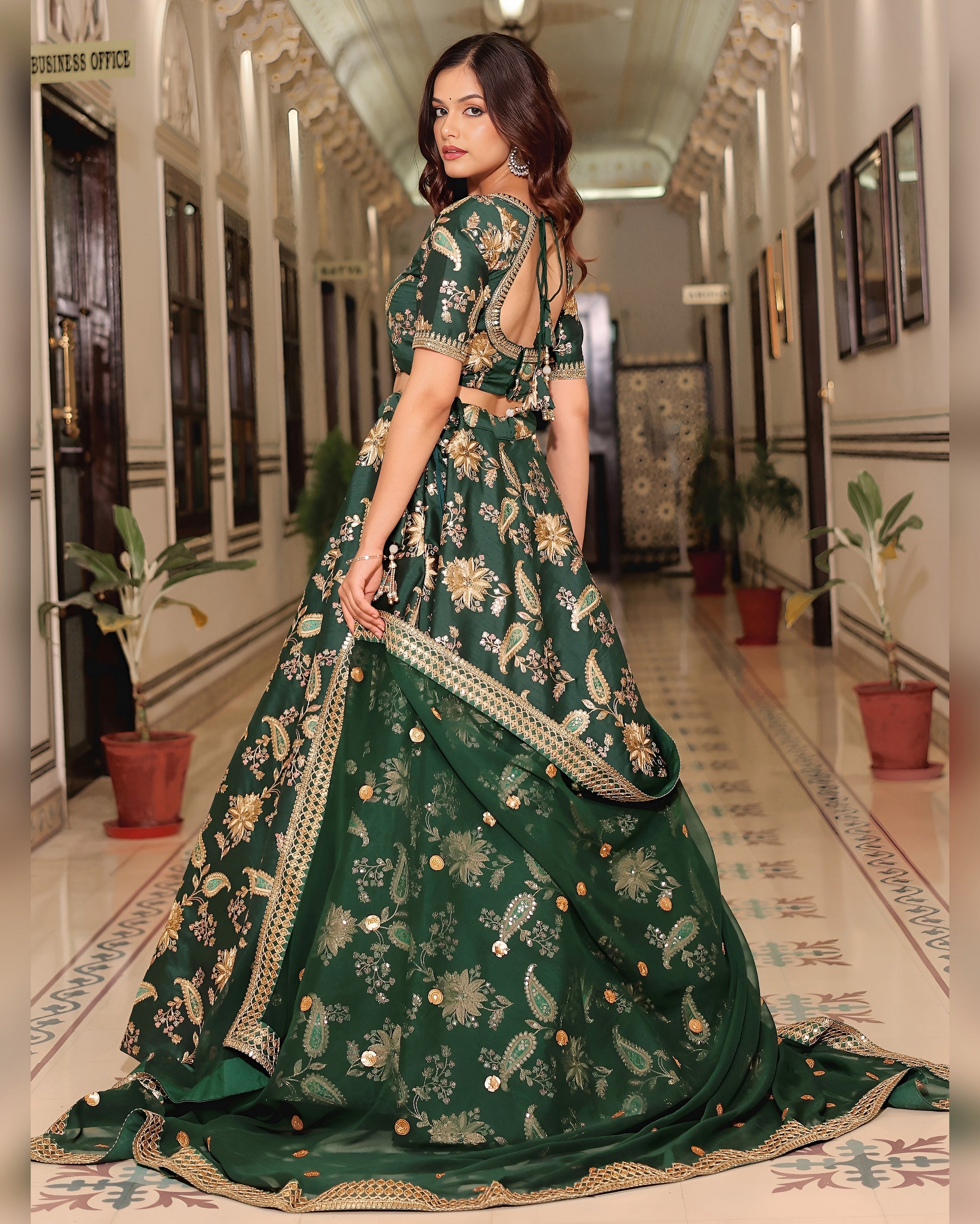 Woman in a green embroidered traditional outfit walking down a hallway.