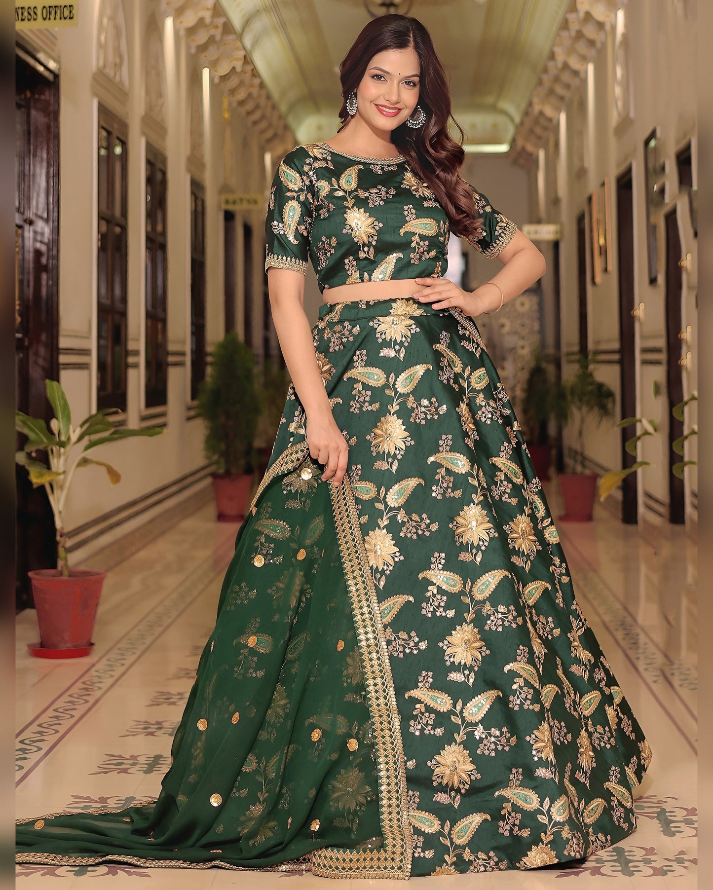 Woman in a green floral dress standing in a hallway with plants.