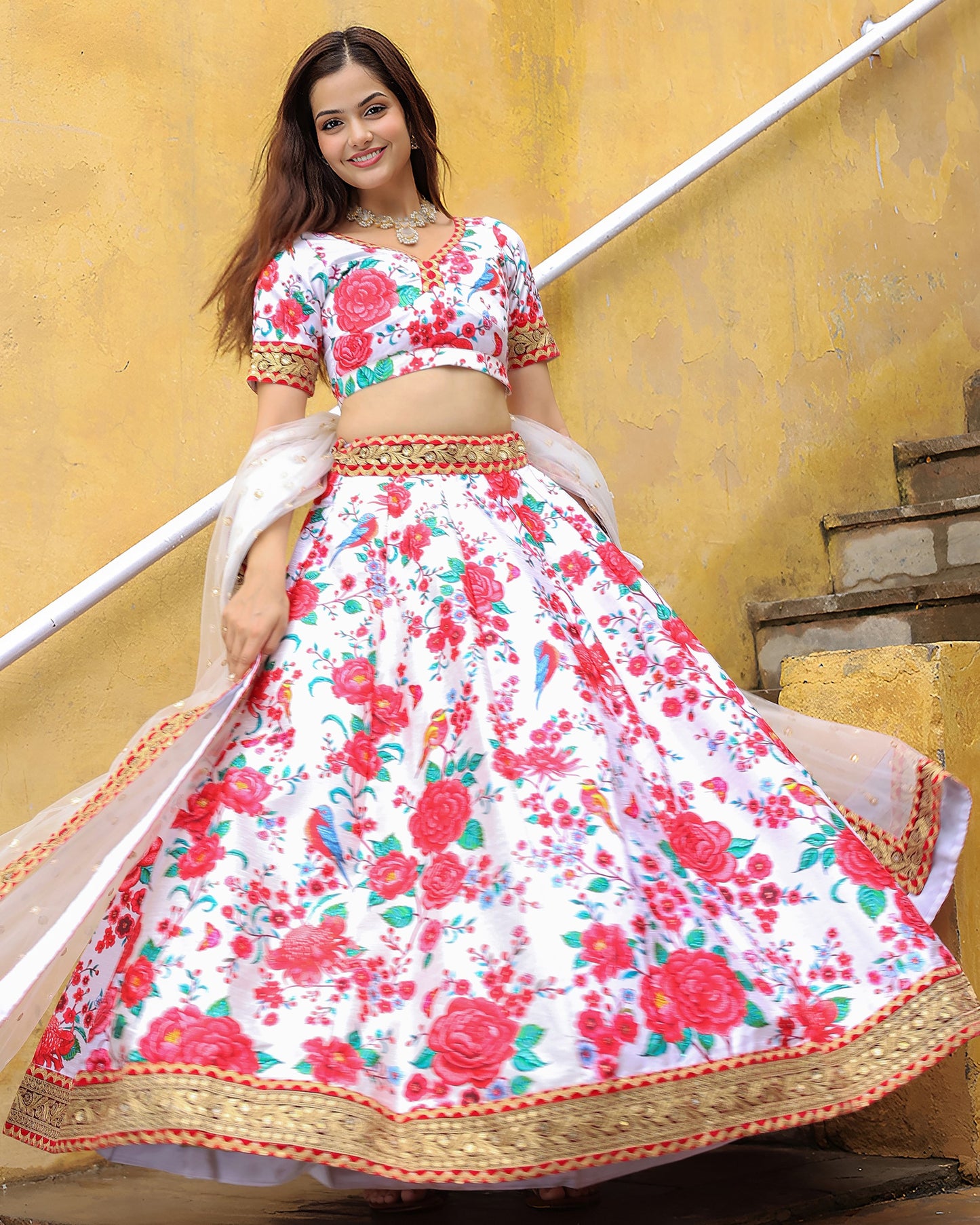 Woman in a floral traditional outfit standing against a yellow wall.