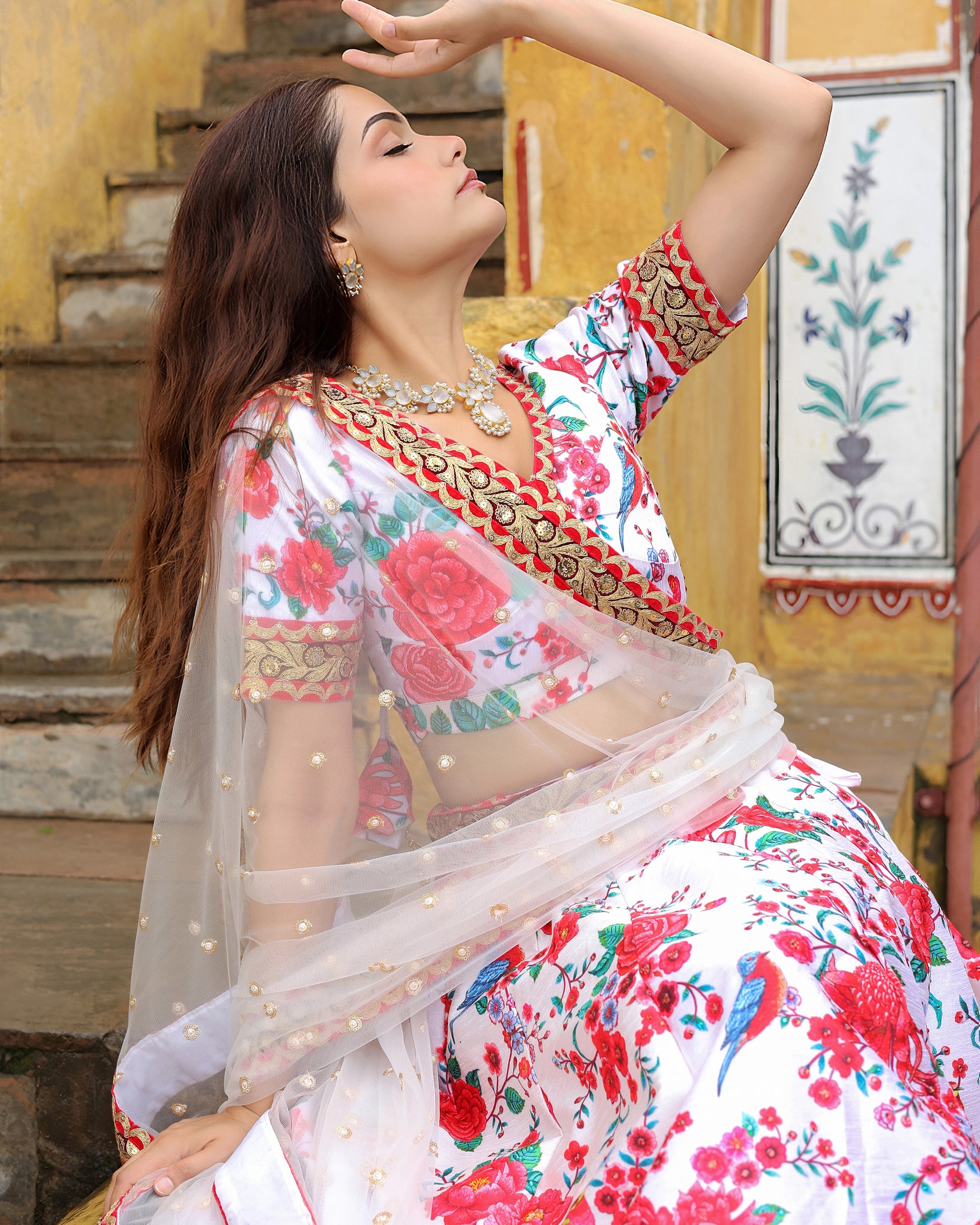 Woman in a floral saree posing on steps with a decorative wall in the background