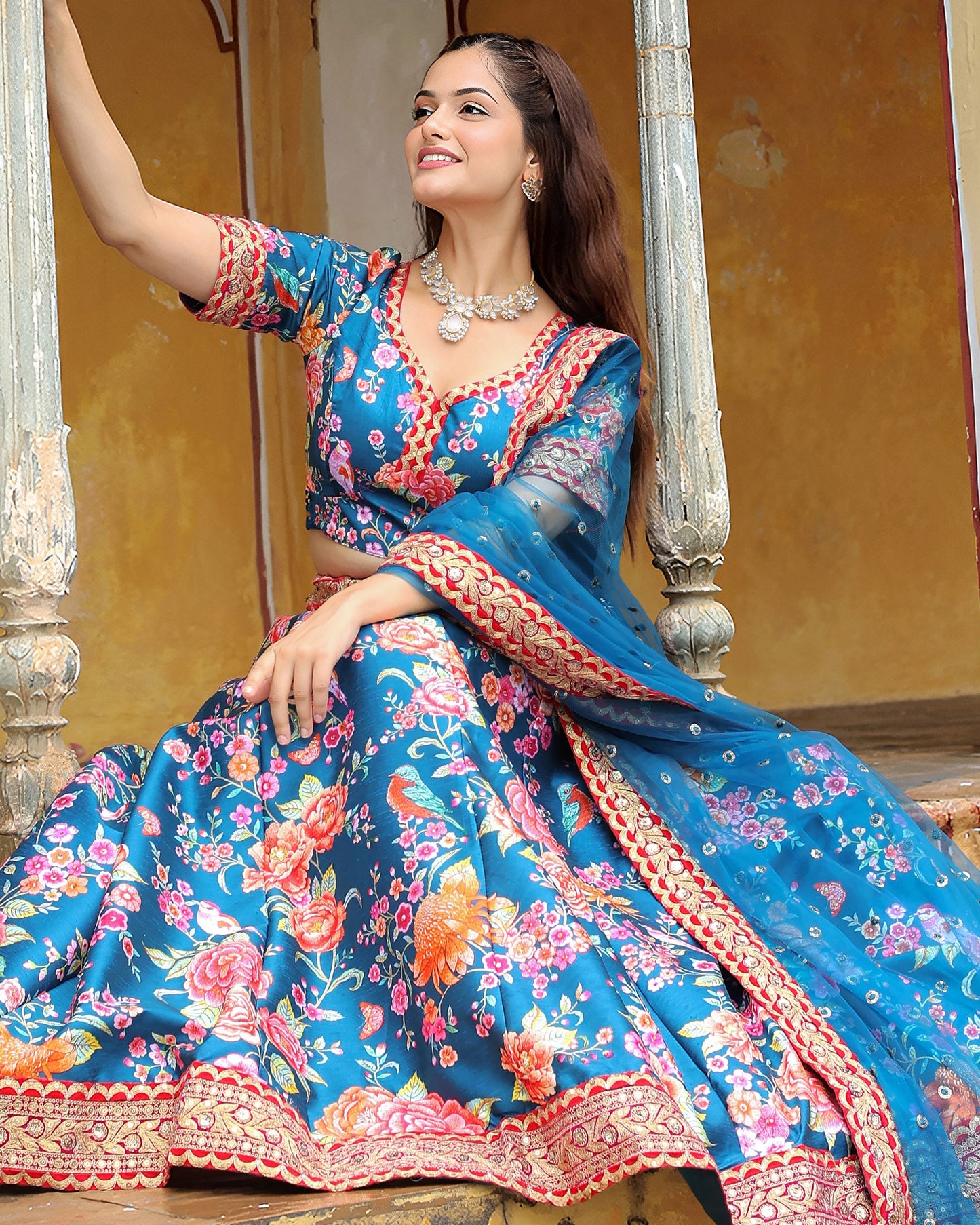Woman in a traditional blue and pink embroidered outfit sitting on a decorative railing.