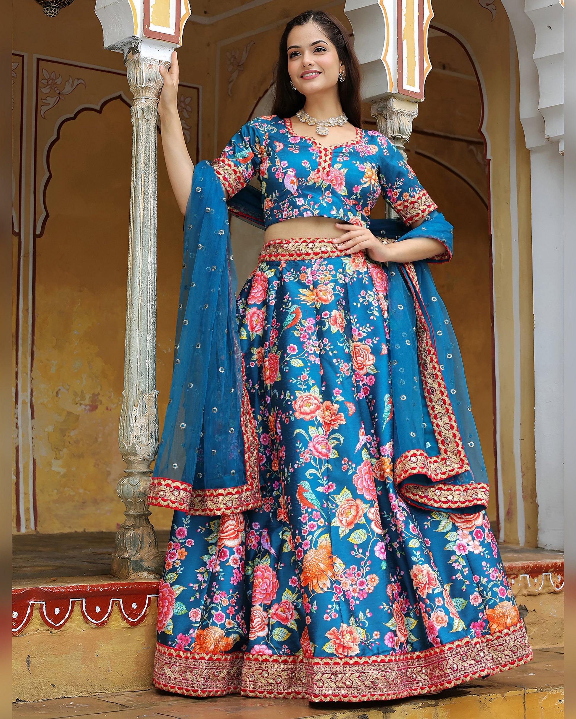 Woman in a traditional blue and floral outfit standing in an ornate indoor setting.