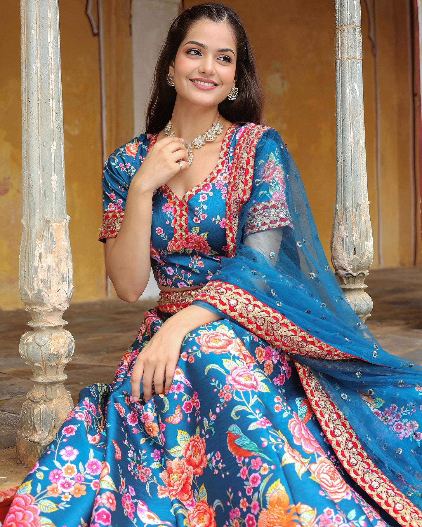 Woman in a colorful traditional outfit with floral patterns sitting on a decorative bench.