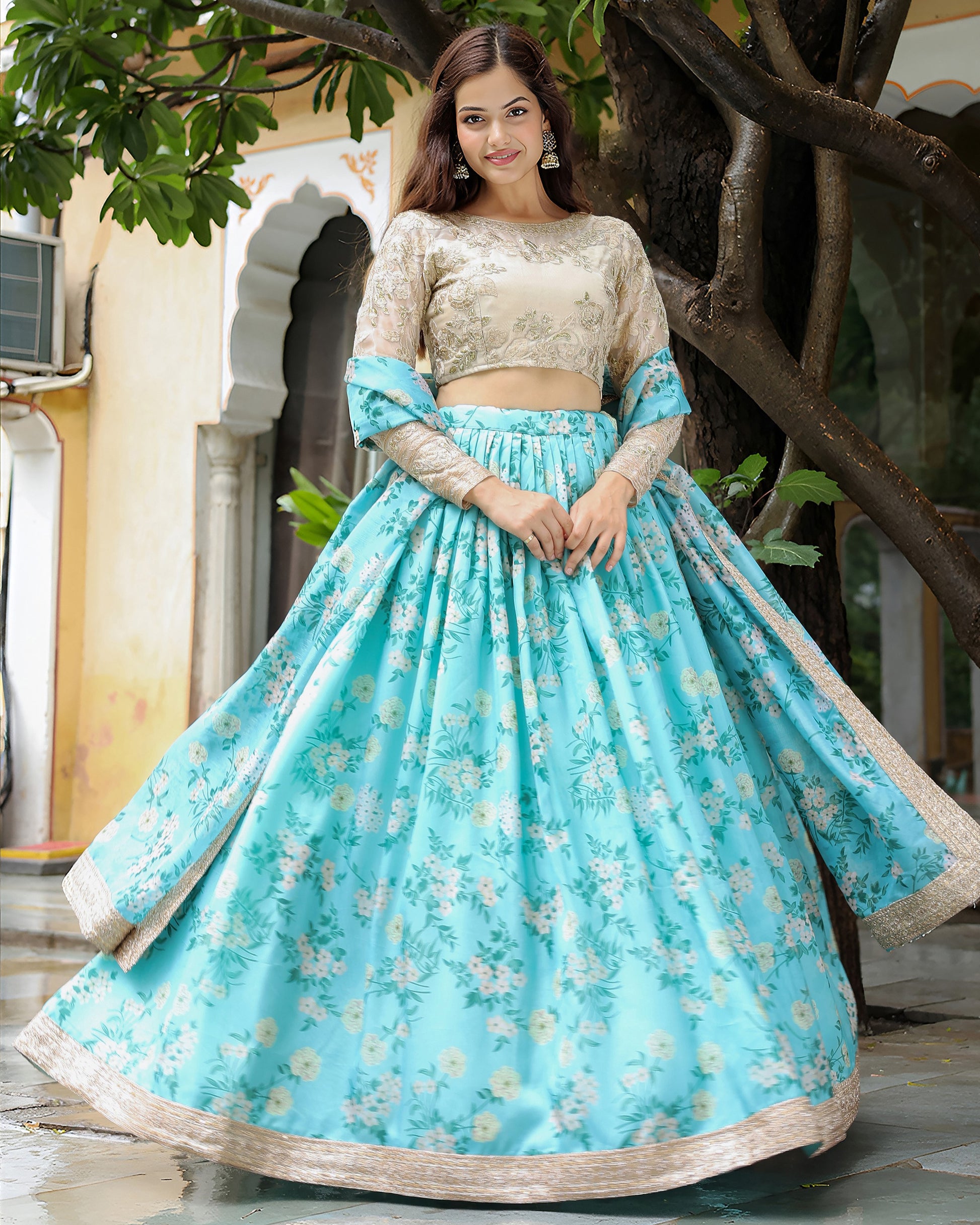 Woman wearing a traditional outfit with a blue floral skirt and beige top, standing outdoors.