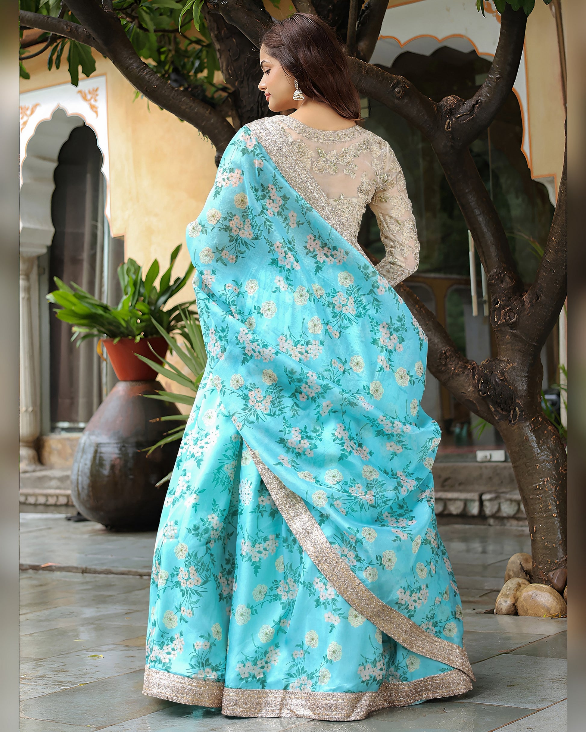 Woman wearing a light blue saree with floral patterns in an outdoor setting.
