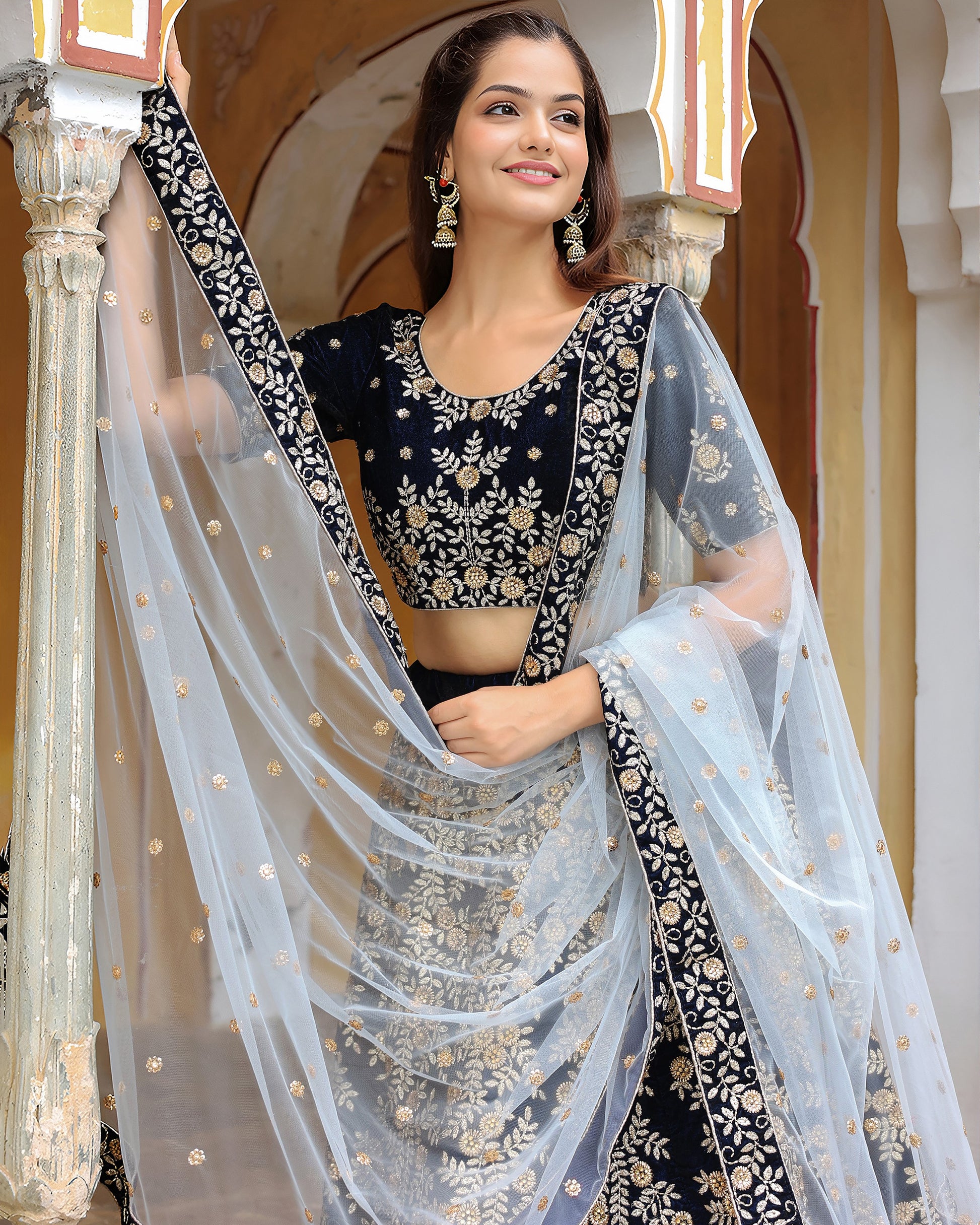 Woman in a traditional black and gold saree with a white dupatta, standing indoors.