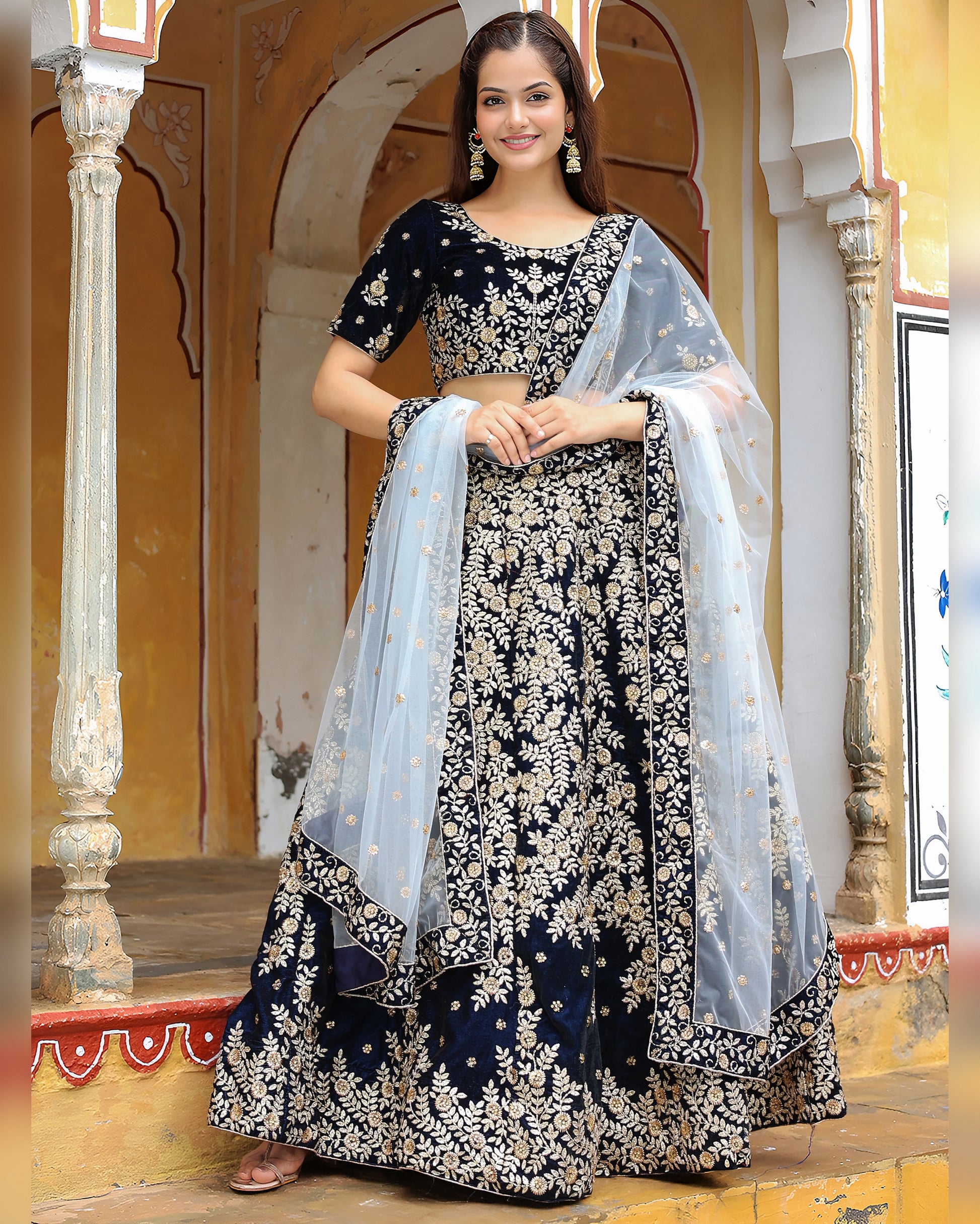 Woman in a traditional black and white embroidered outfit with a sheer dupatta in a decorative setting.