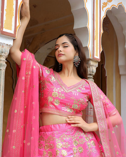 Woman in a pink traditional outfit with gold embroidery standing in front of an architectural background.