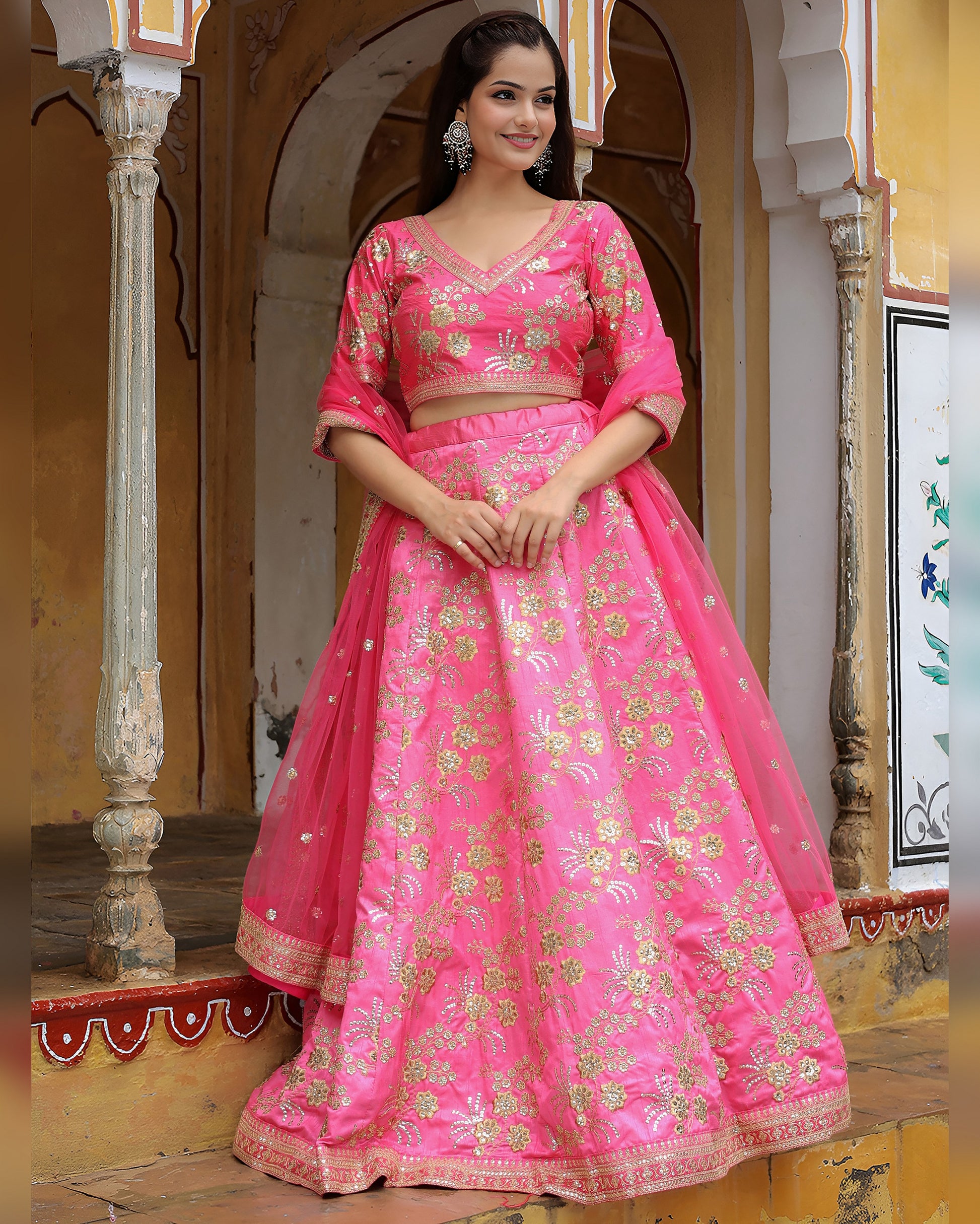 Woman in a pink traditional outfit standing in an ornate indoor setting.