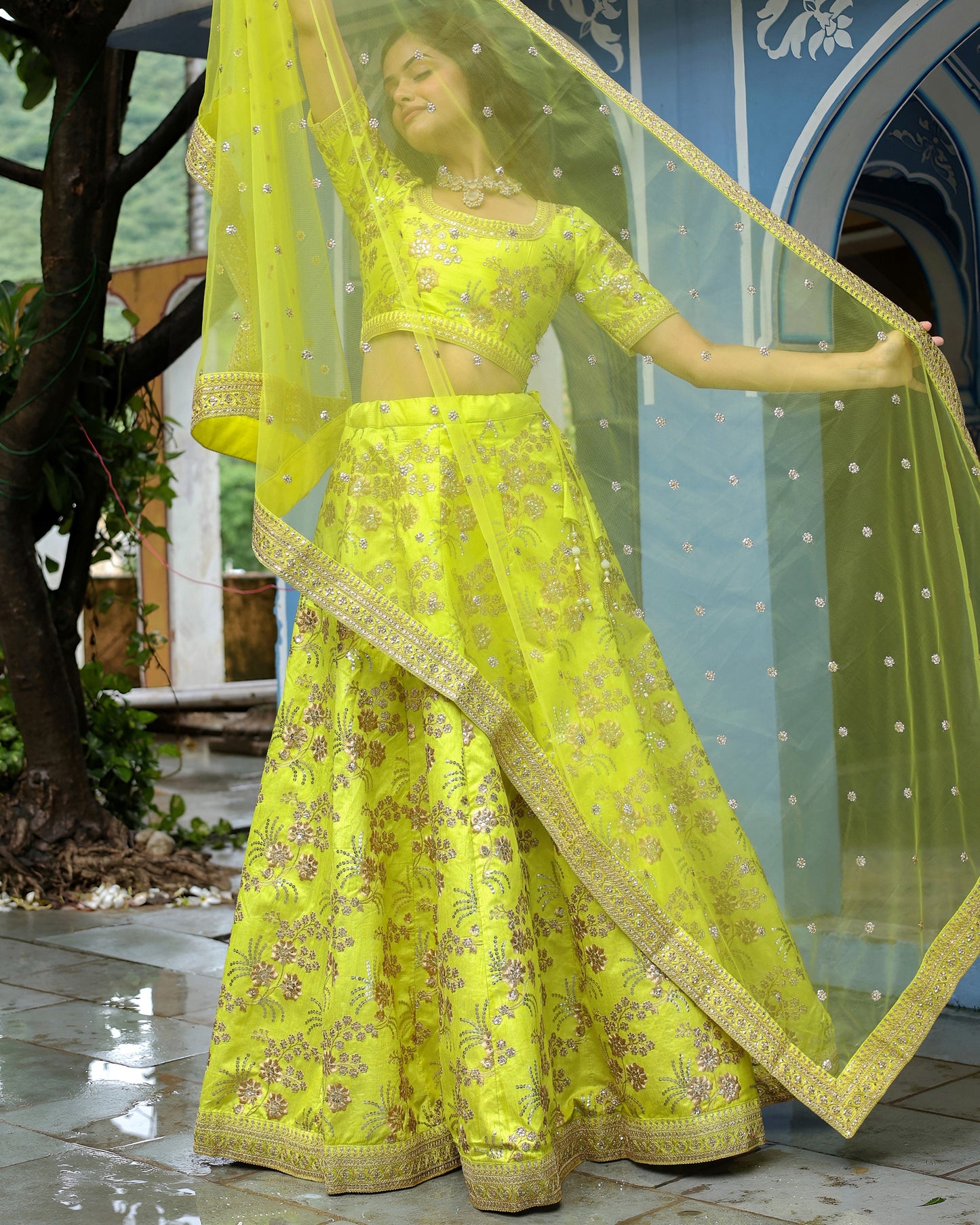 Woman in a bright yellow traditional outfit with floral patterns, standing outdoors.
